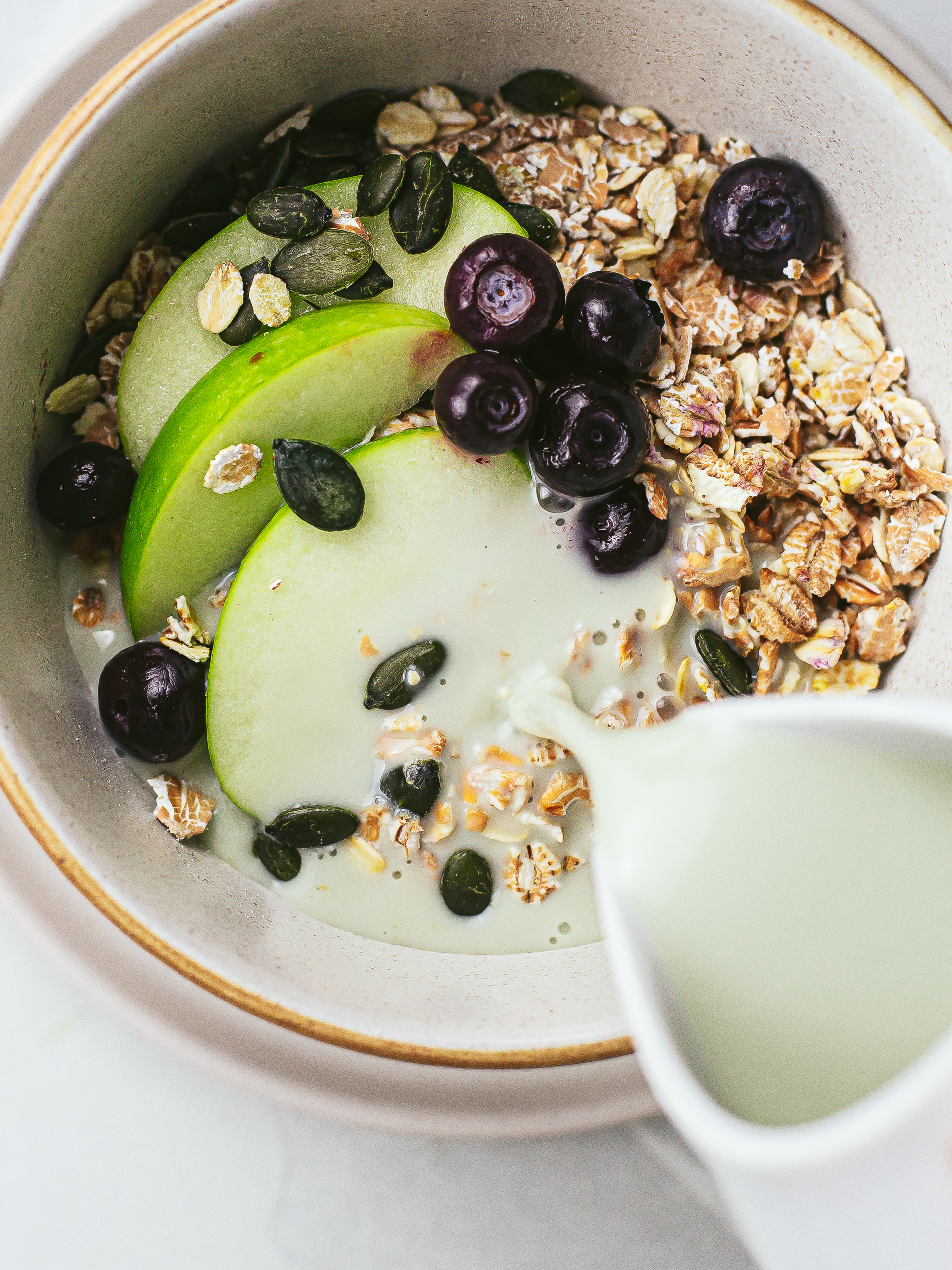 homemade pumpkin seed milk poured in a bowl with muesli and fruit
