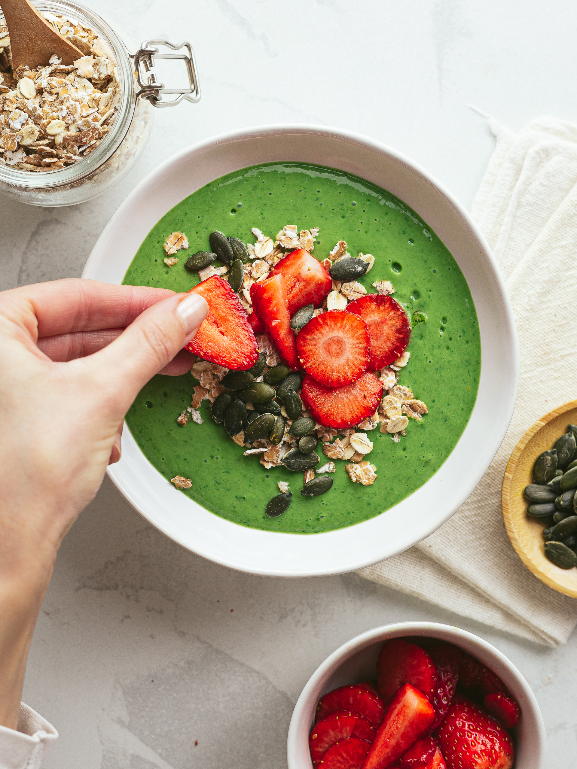 high-iron spinach smoothie in a bowl topped with oats, strawberries and pumpkin seeds