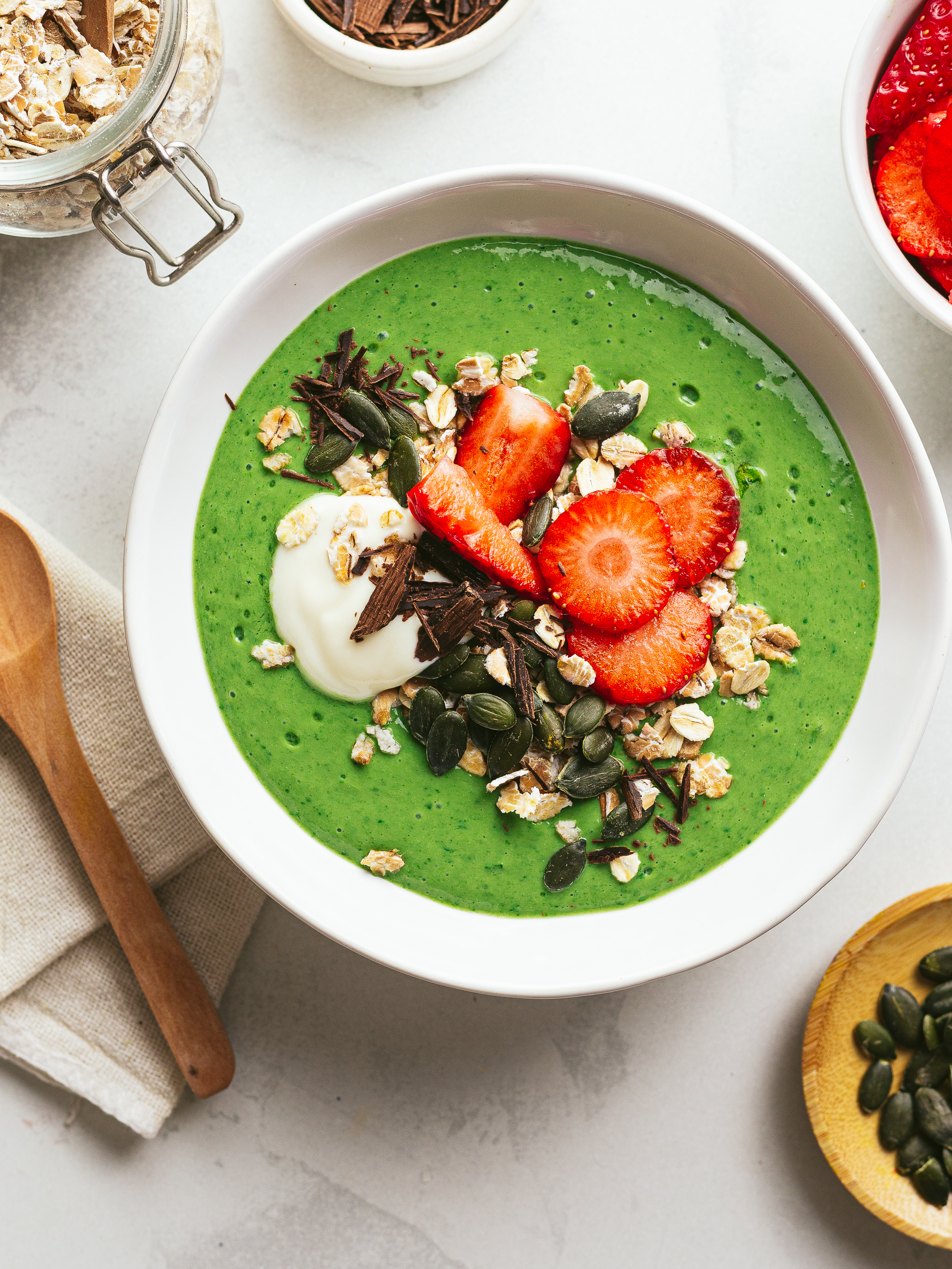 green spinach smoothie bowl with strawberries, oats, and dark chocolate