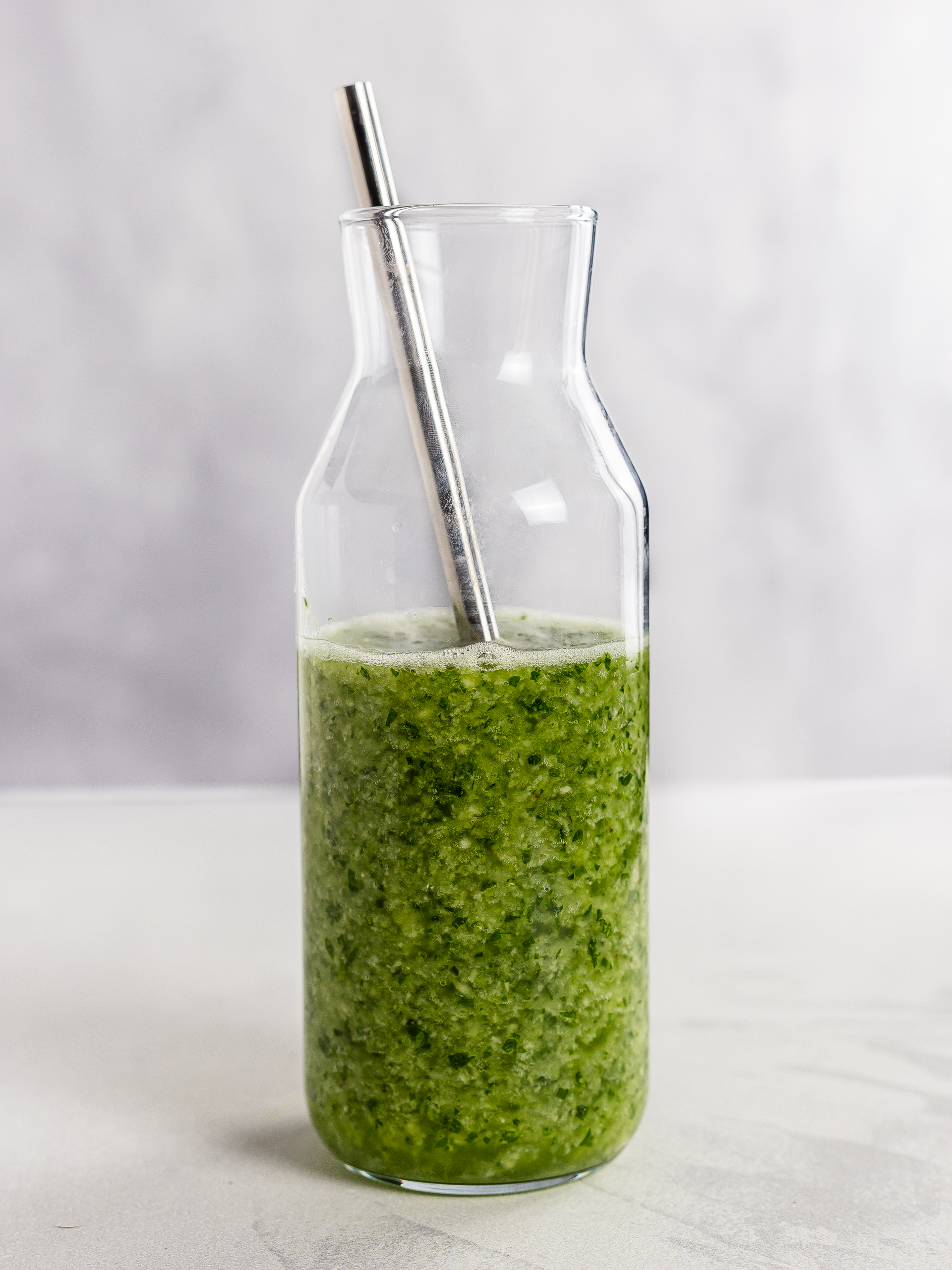 parsley smoothie in a jug with a straw