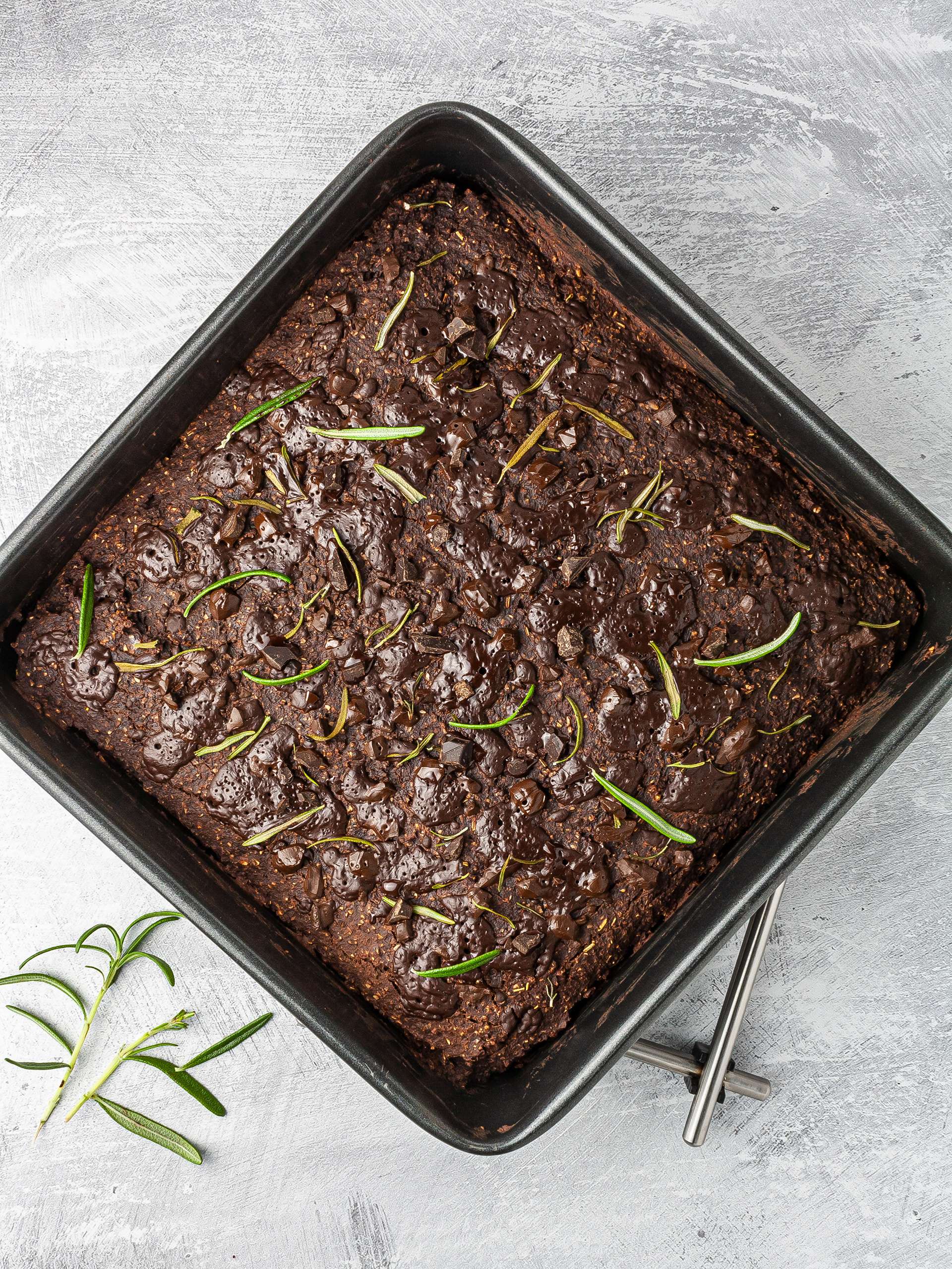 Baked rosemary brownies with chocolate chunks and rosemary leaves.