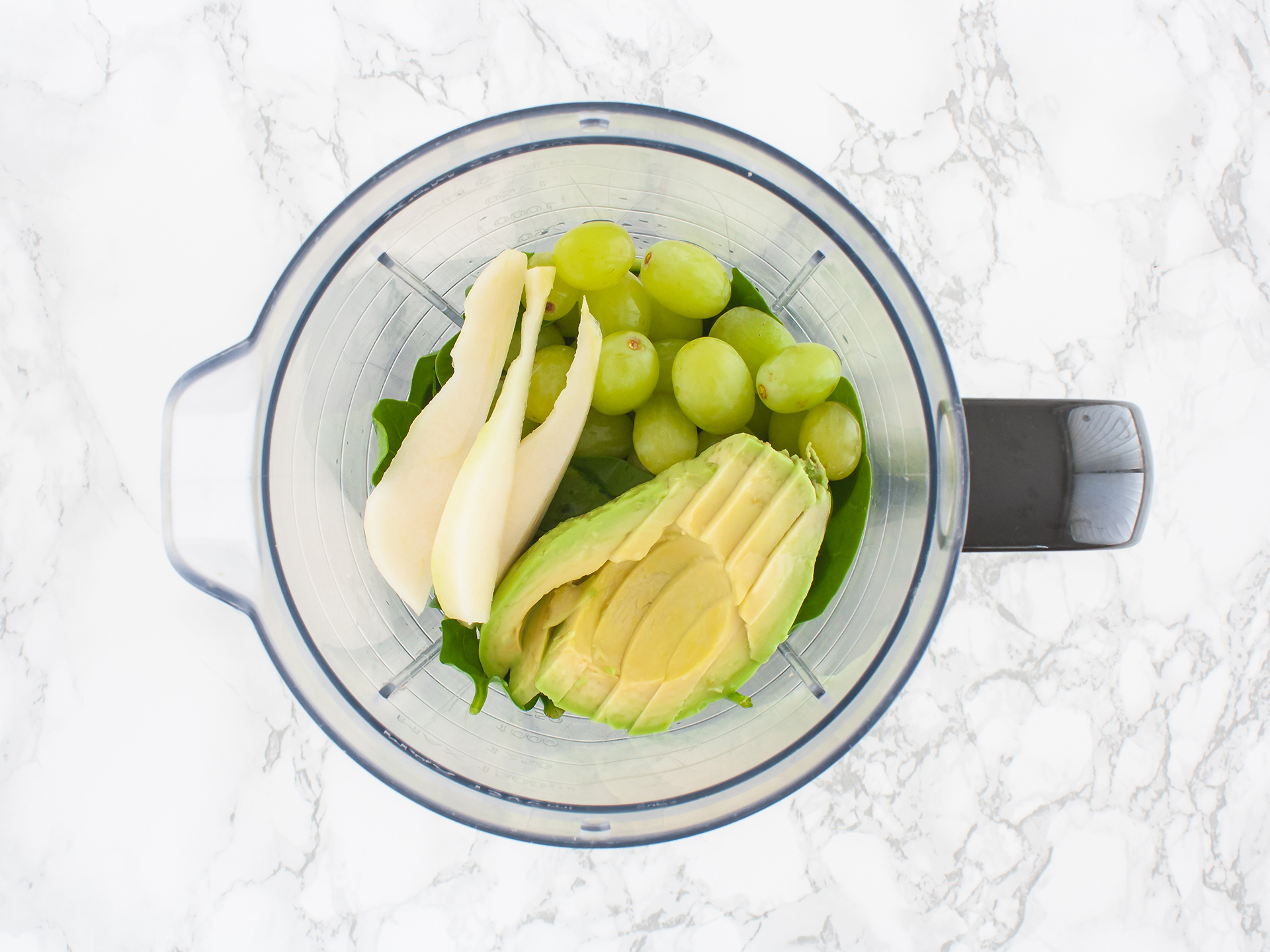 Spinach, avocado, pears, and grapes in a food processor.