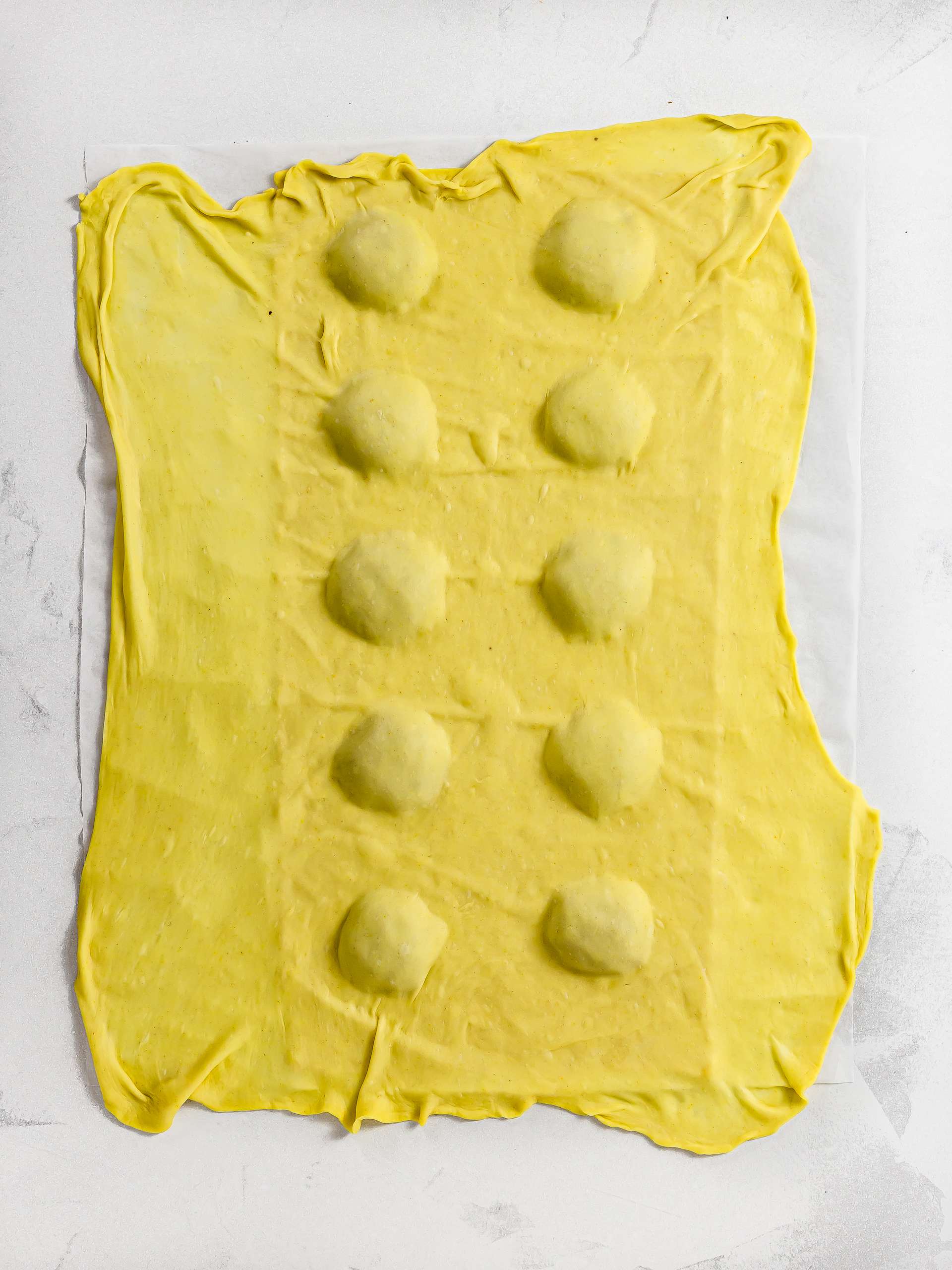 one sheet of pasta dough draped over another sheet with ravioli filling