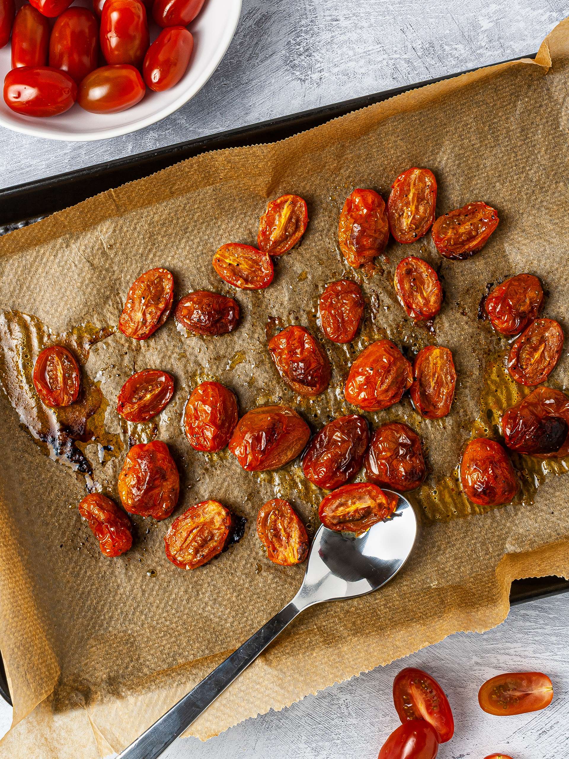 Whole and halved cherry tomatoes roasted with olive oil over a baking tray