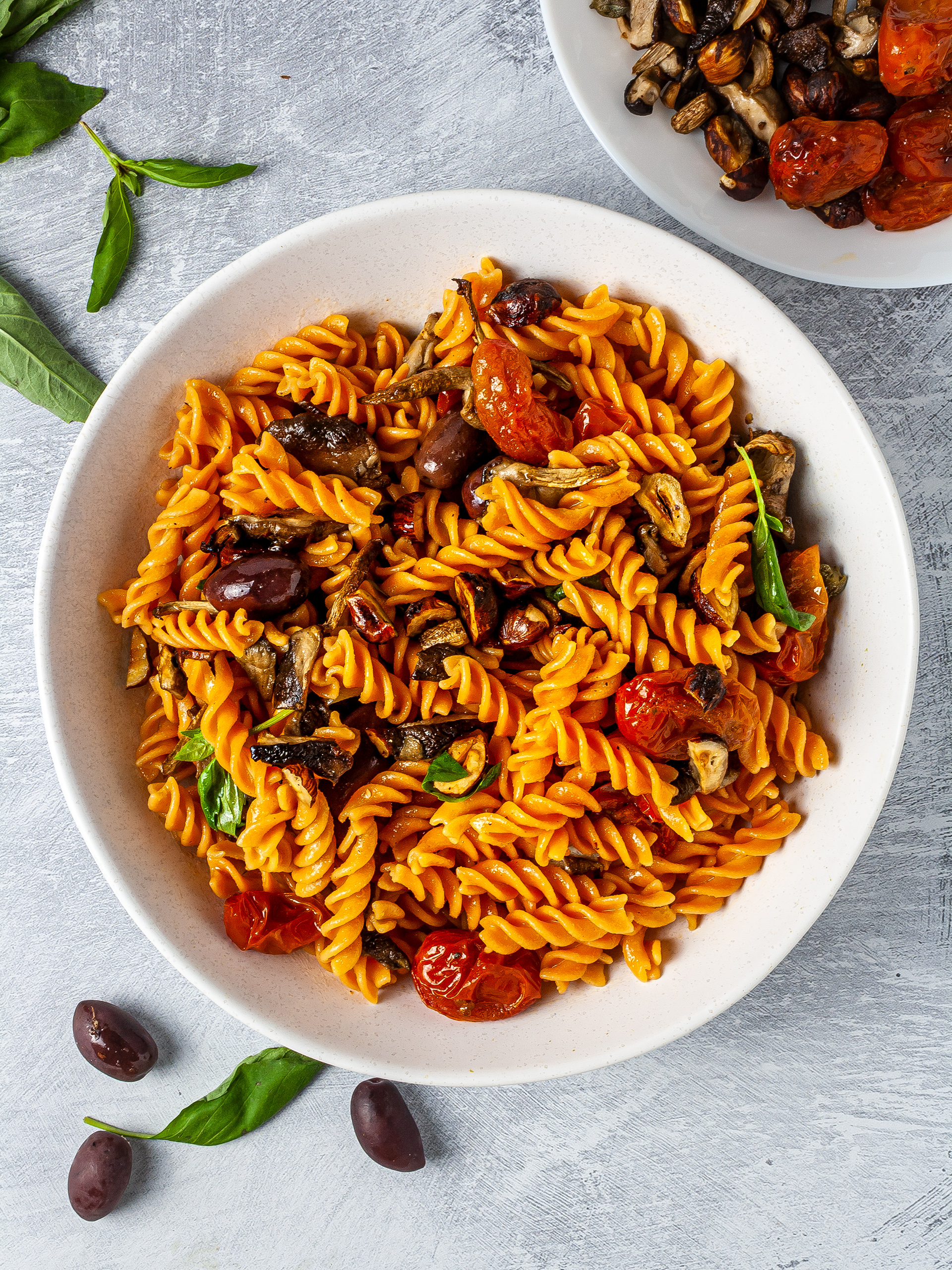 Bowl of pasta salad with fresh basil, olives, roasted cherry tomatoes, 