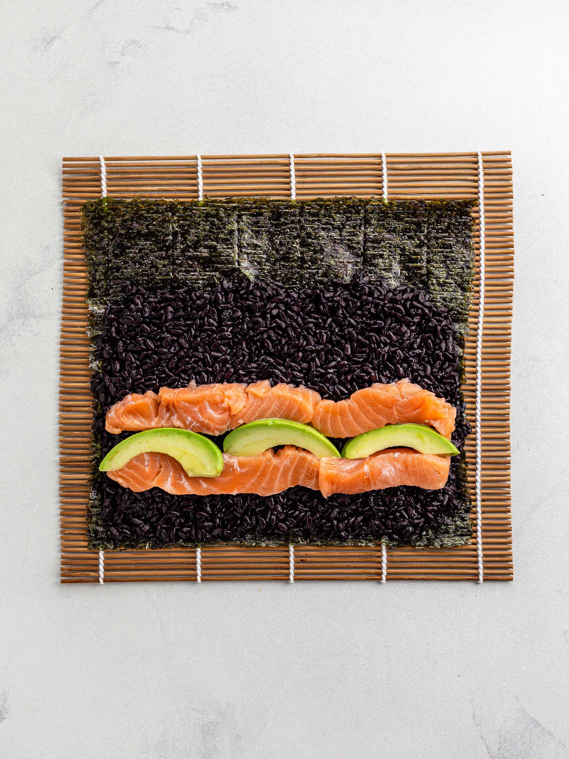 salmon avocado black rice sushi on a mat