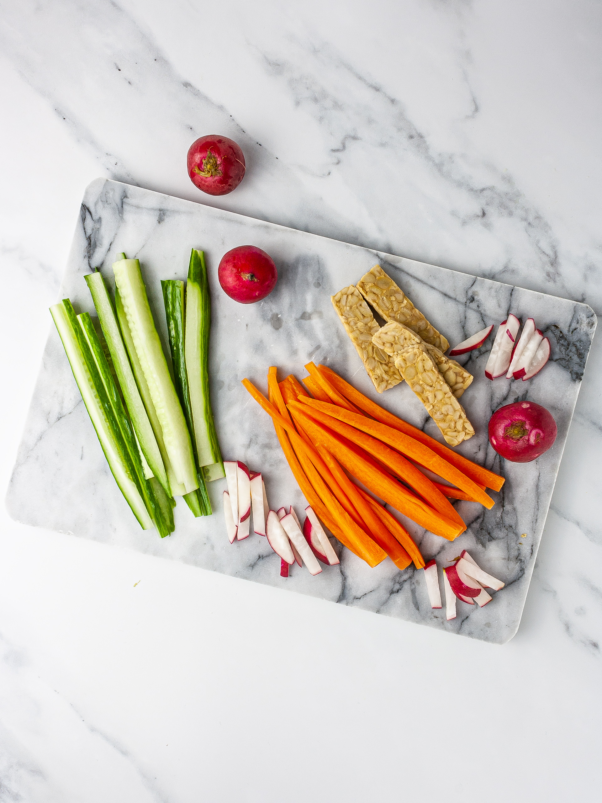 Slice vegetables including cucumber, carrots and radishes, and sliced tempeh.