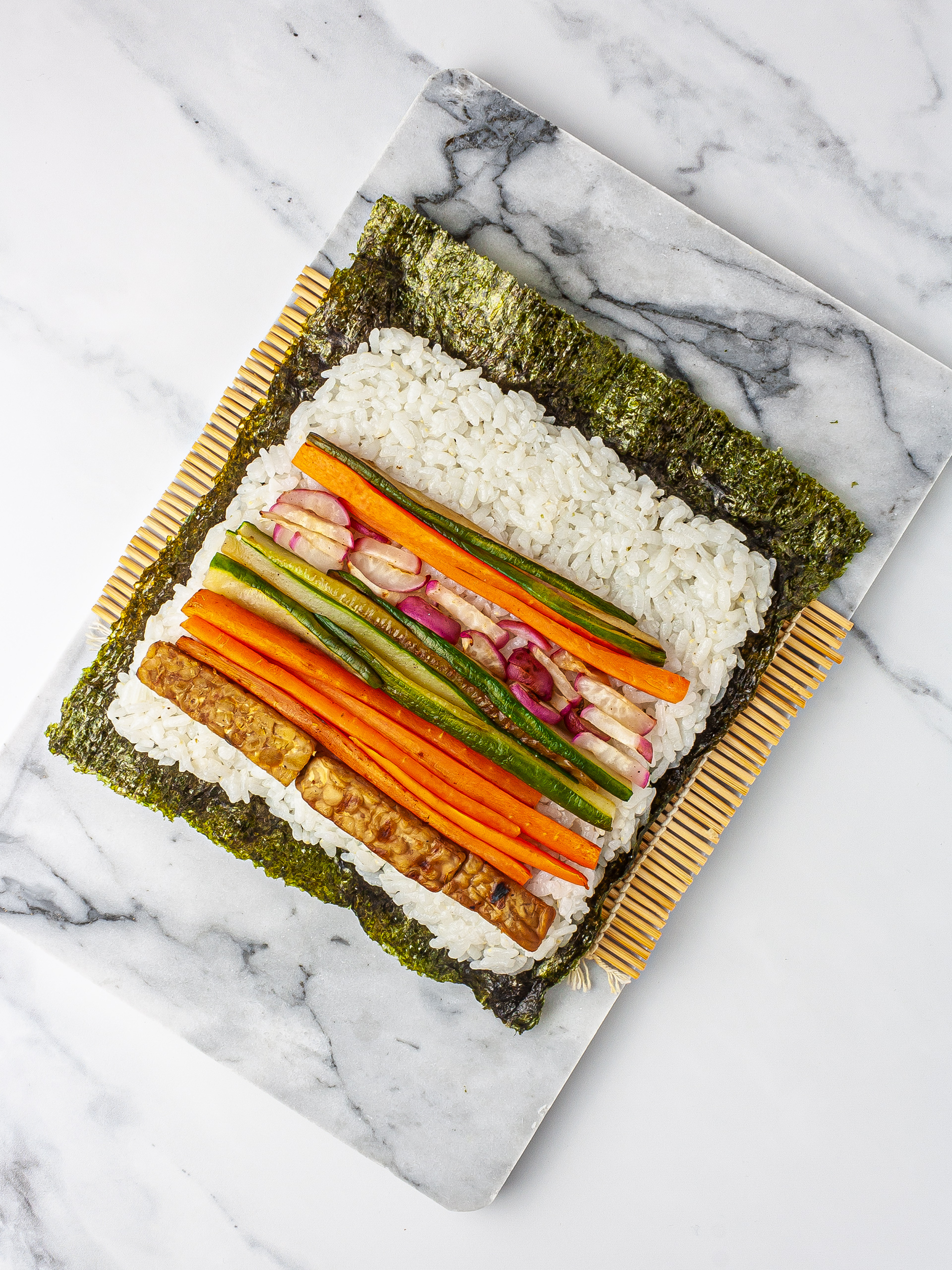 Nori sheet with sushi rice, vegetables, and tempeh on a sushi mat.