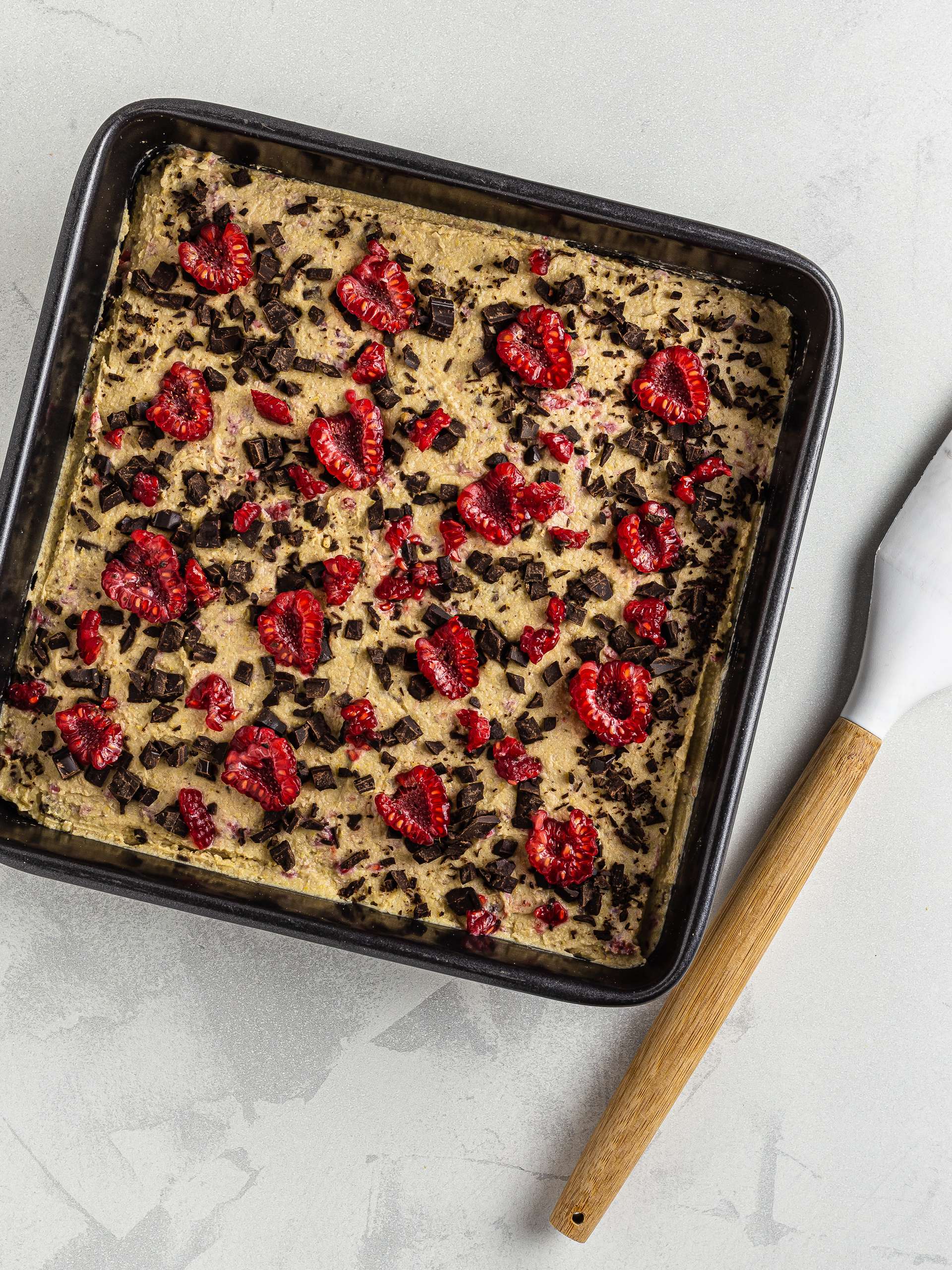 chickpea blondie dough in a square baking tray with raspberries and chocolate chips