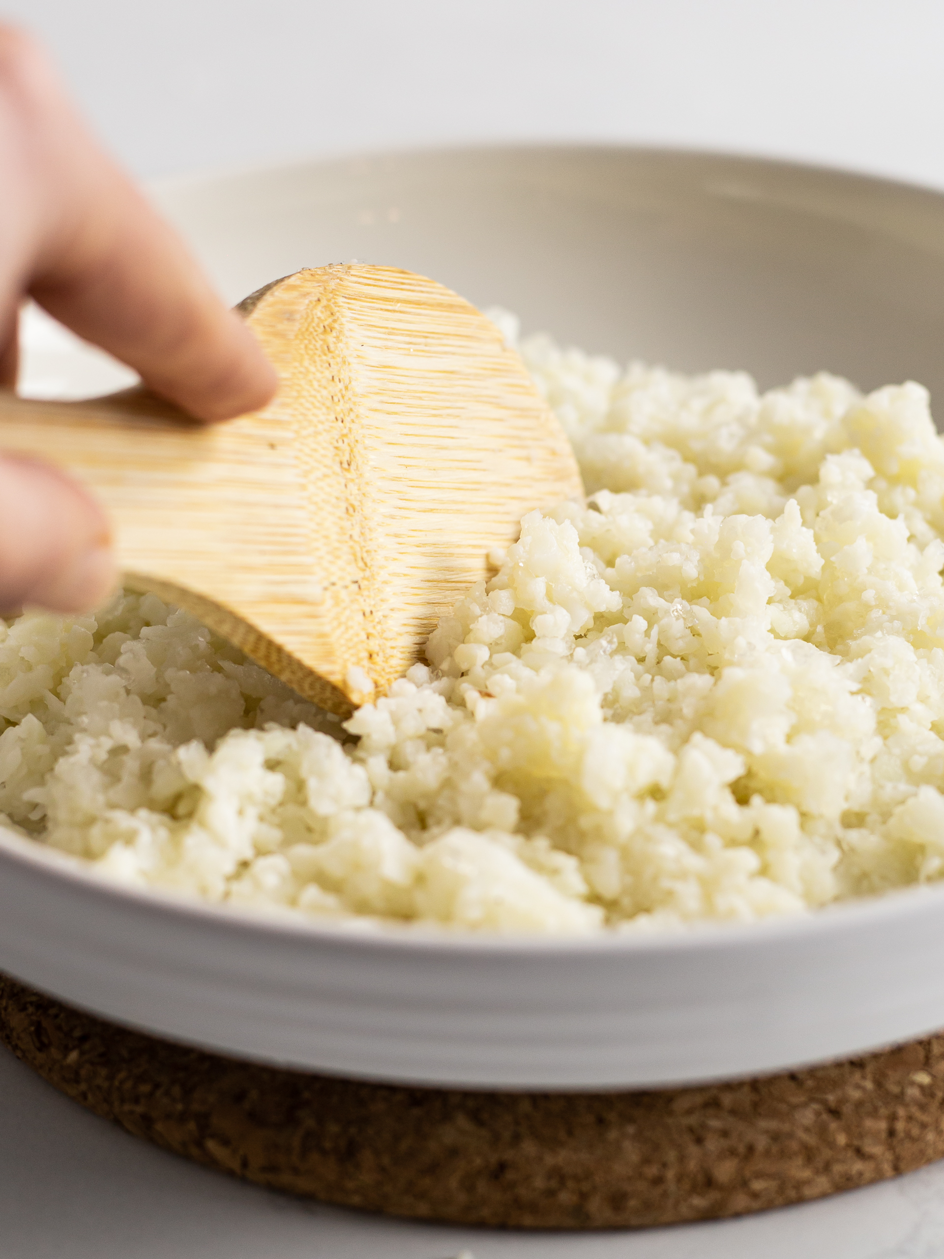 sticky cauliflower rice in a bowl mixed with a wooden spatula