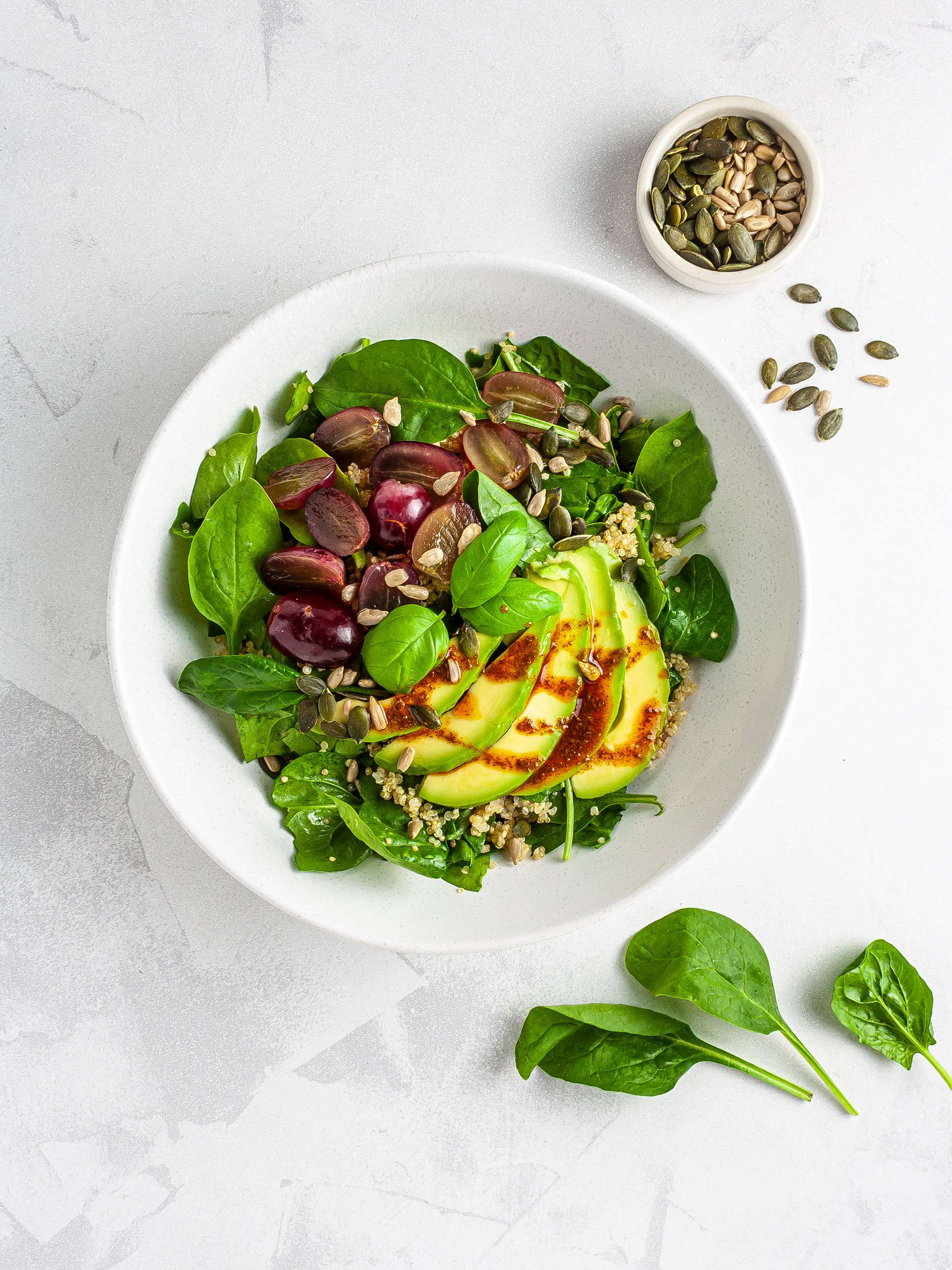 Spinach, grapes, quinoa, and avocado in a salad bowl topped with seeds and dressing