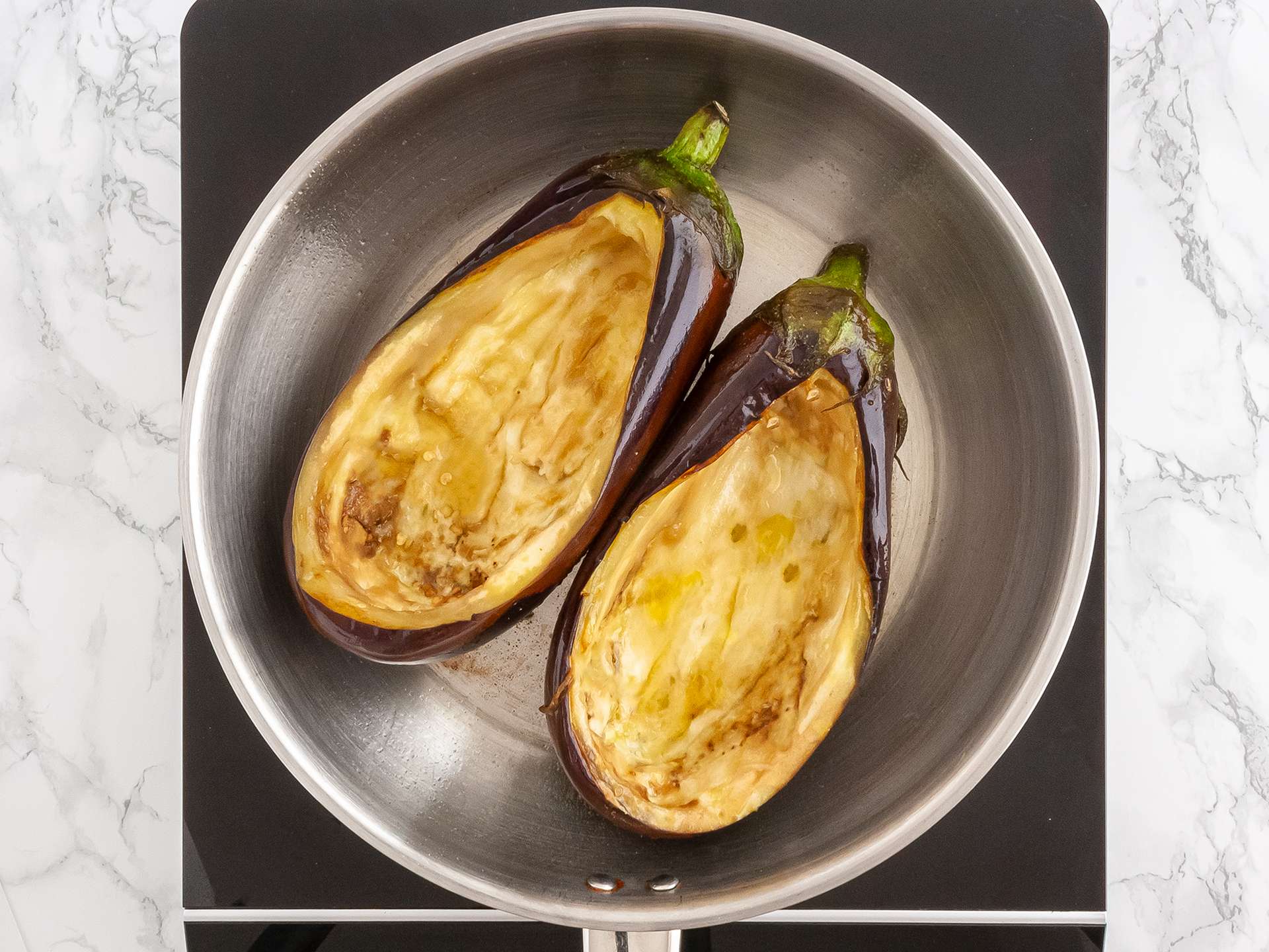 Two aubergines sliced and carved cooking in  a pan