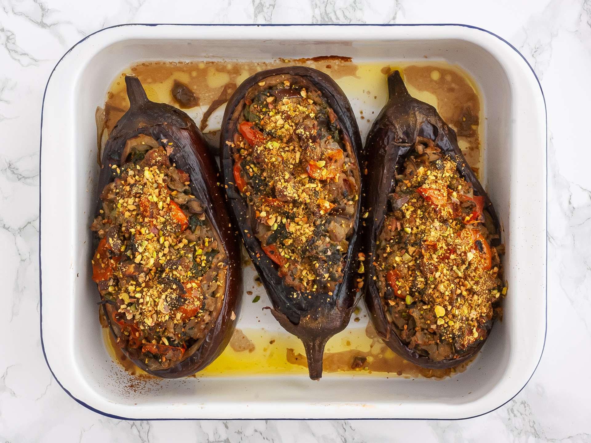 Cooked keto aubergines in a roasting tin sprinkled with roasted pistachios