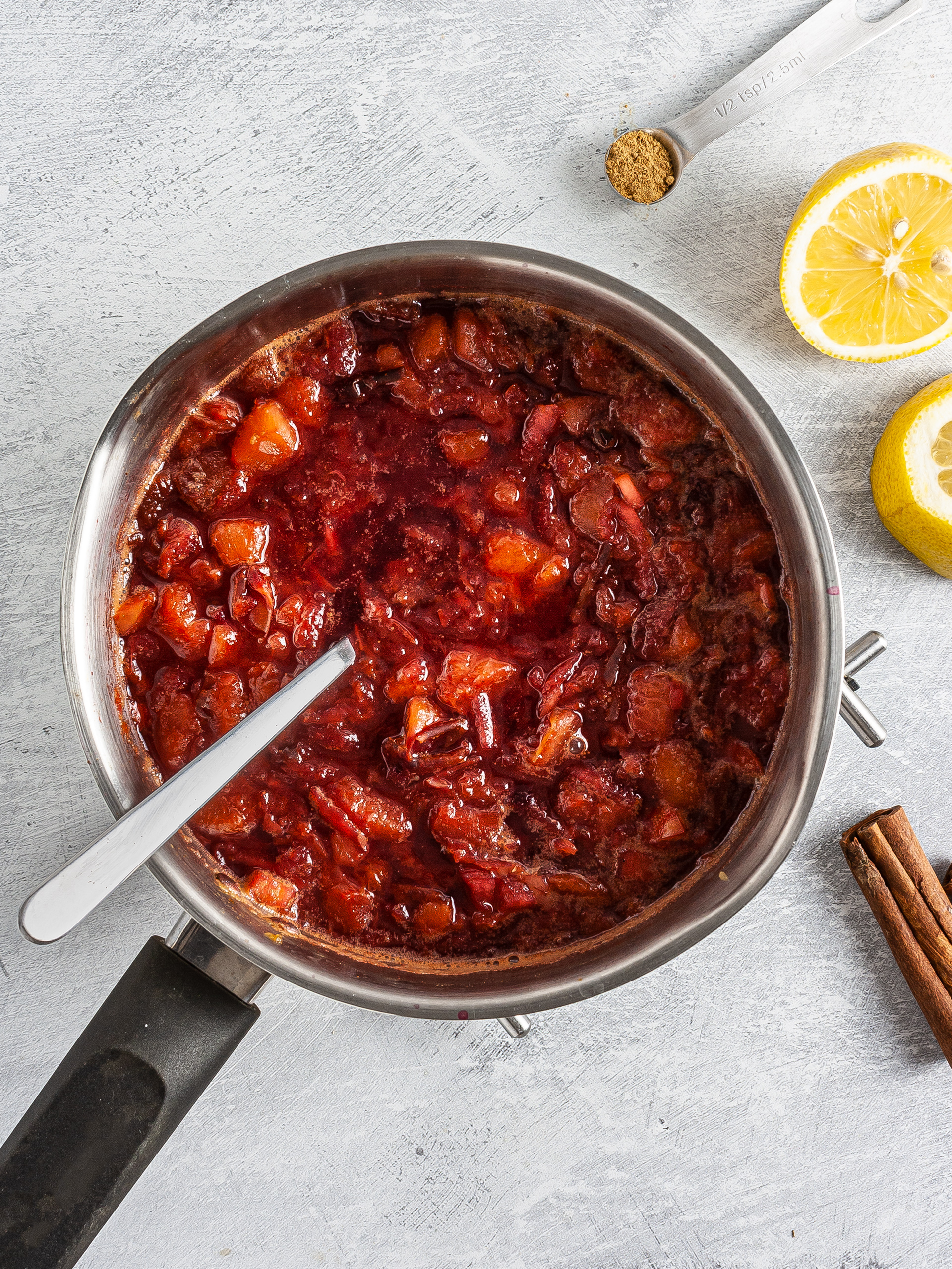 Plums, apple, cinnamon, and lemon cooking in a pan.