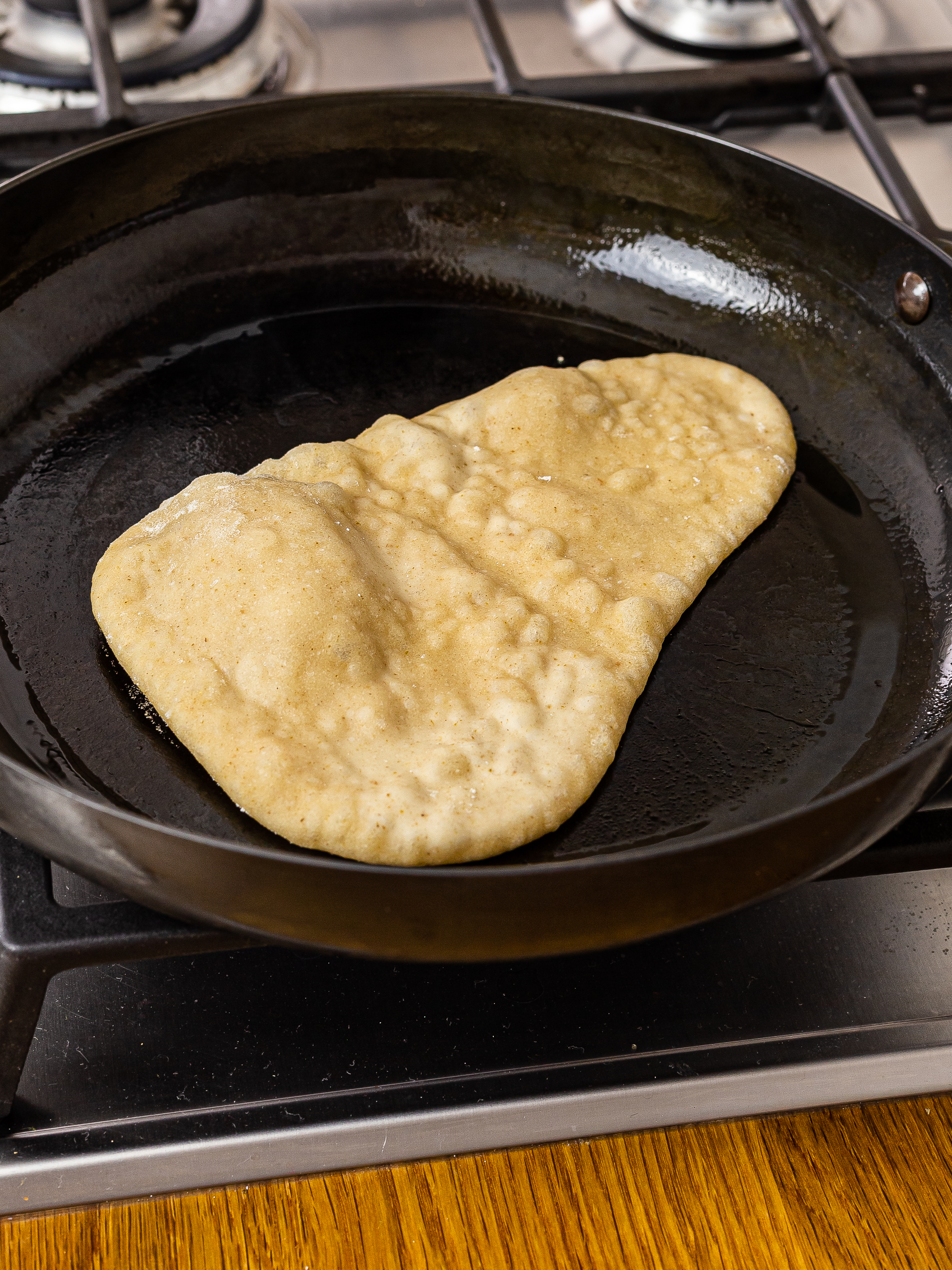 sourdough naan cooking in a cast iron skillet