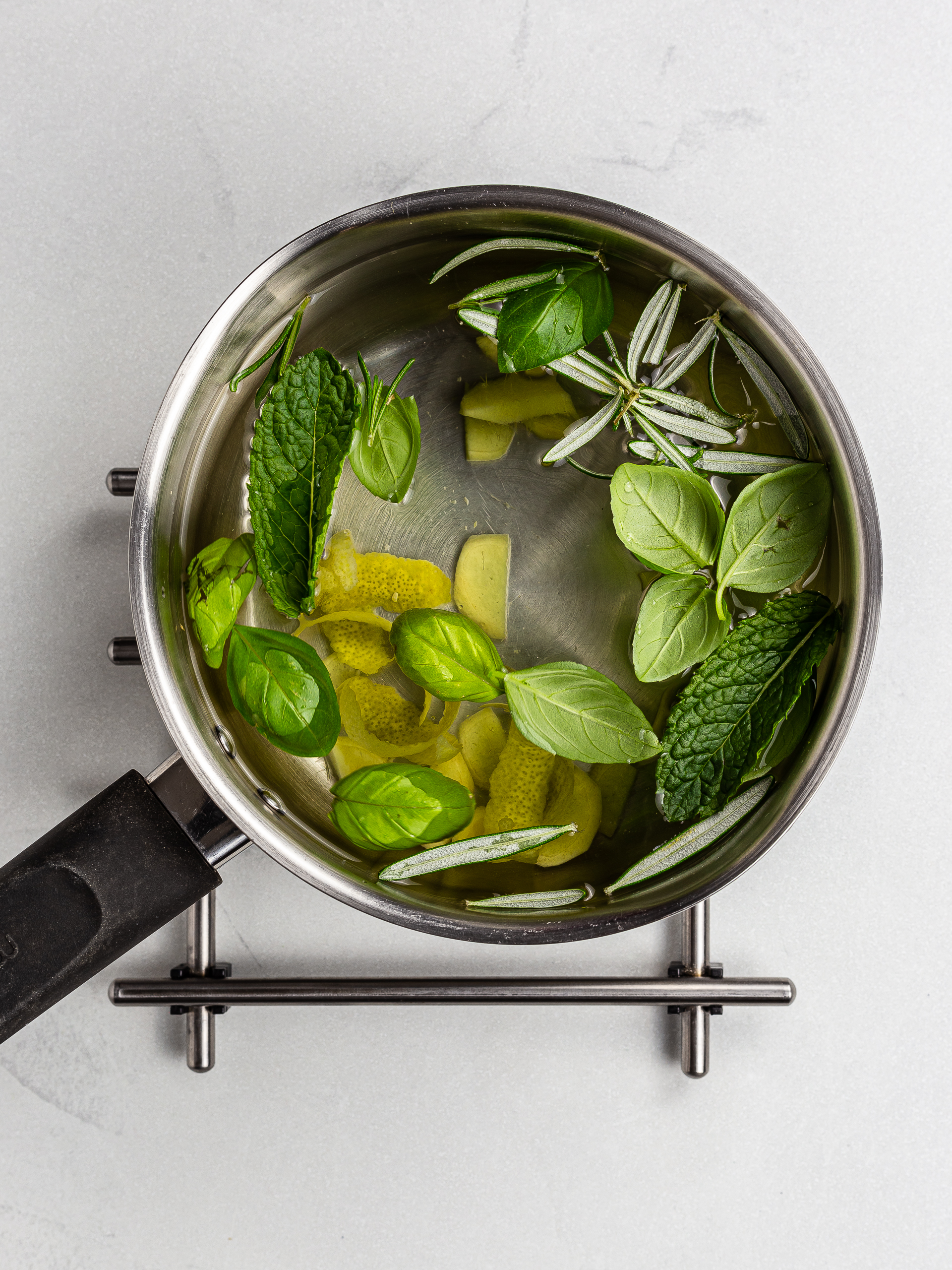 fresh herbs in a pot of water with ginger and lemon peel