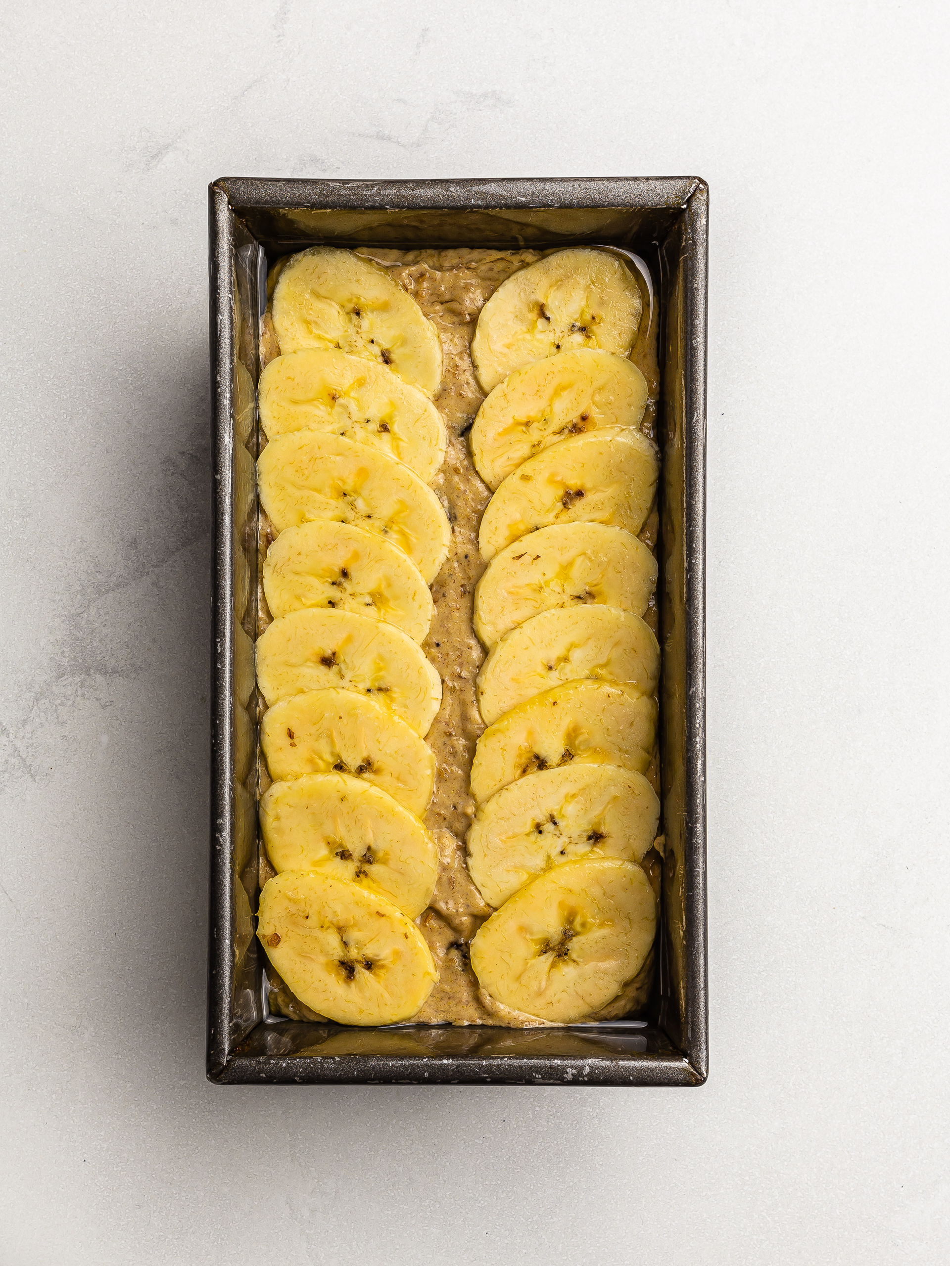 vegan plantain bread batter in a loaf tin topped with plantain chips