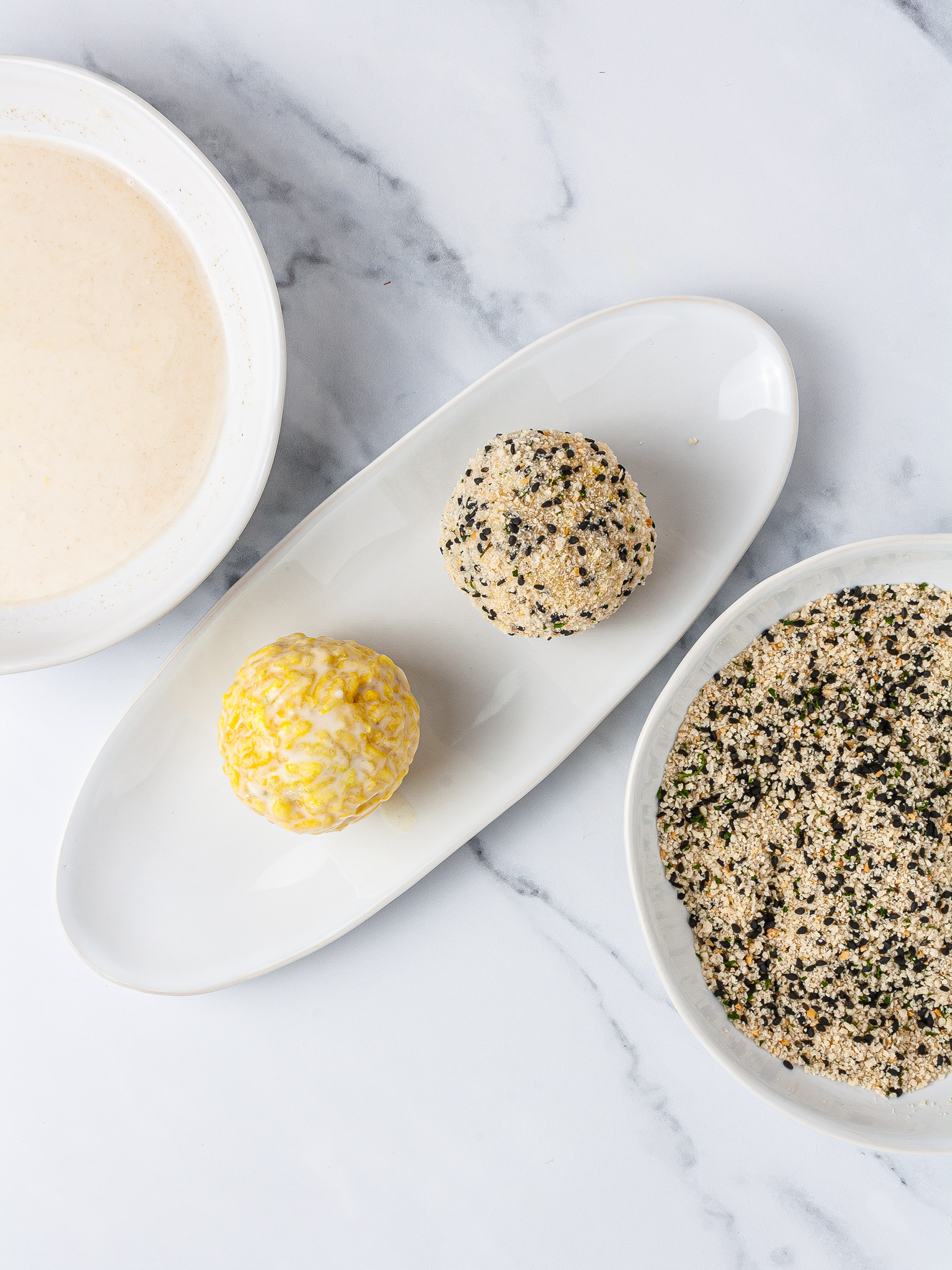 Coating the arancini with flour batter, breadcrumbs, and sesame seeds.