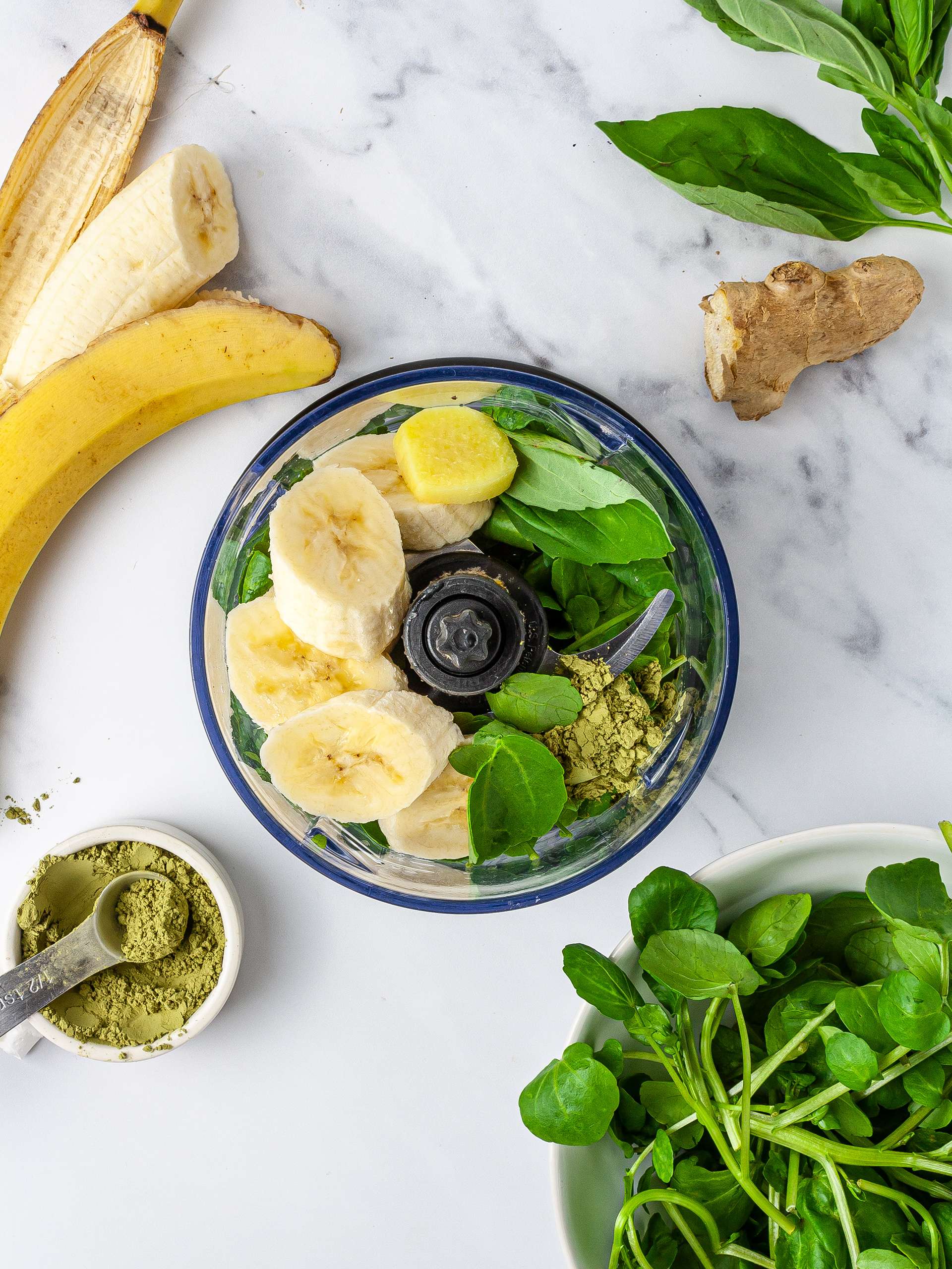 Bananas, watercress, basil, ginger, matcha powder in a food processor for green smoothie.