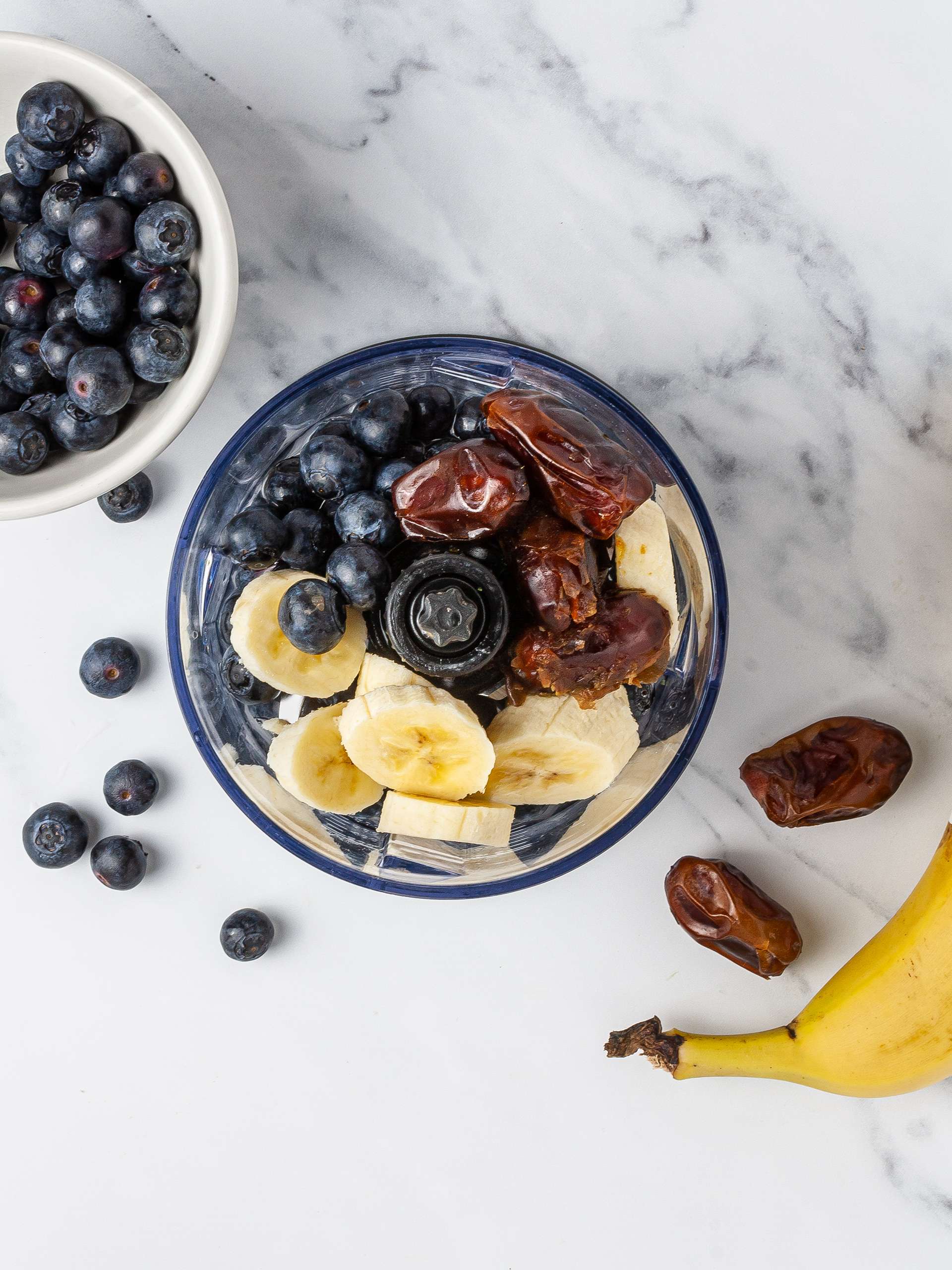Bananas, dates, blueberries, and coconut water in a food processor for smoothie.