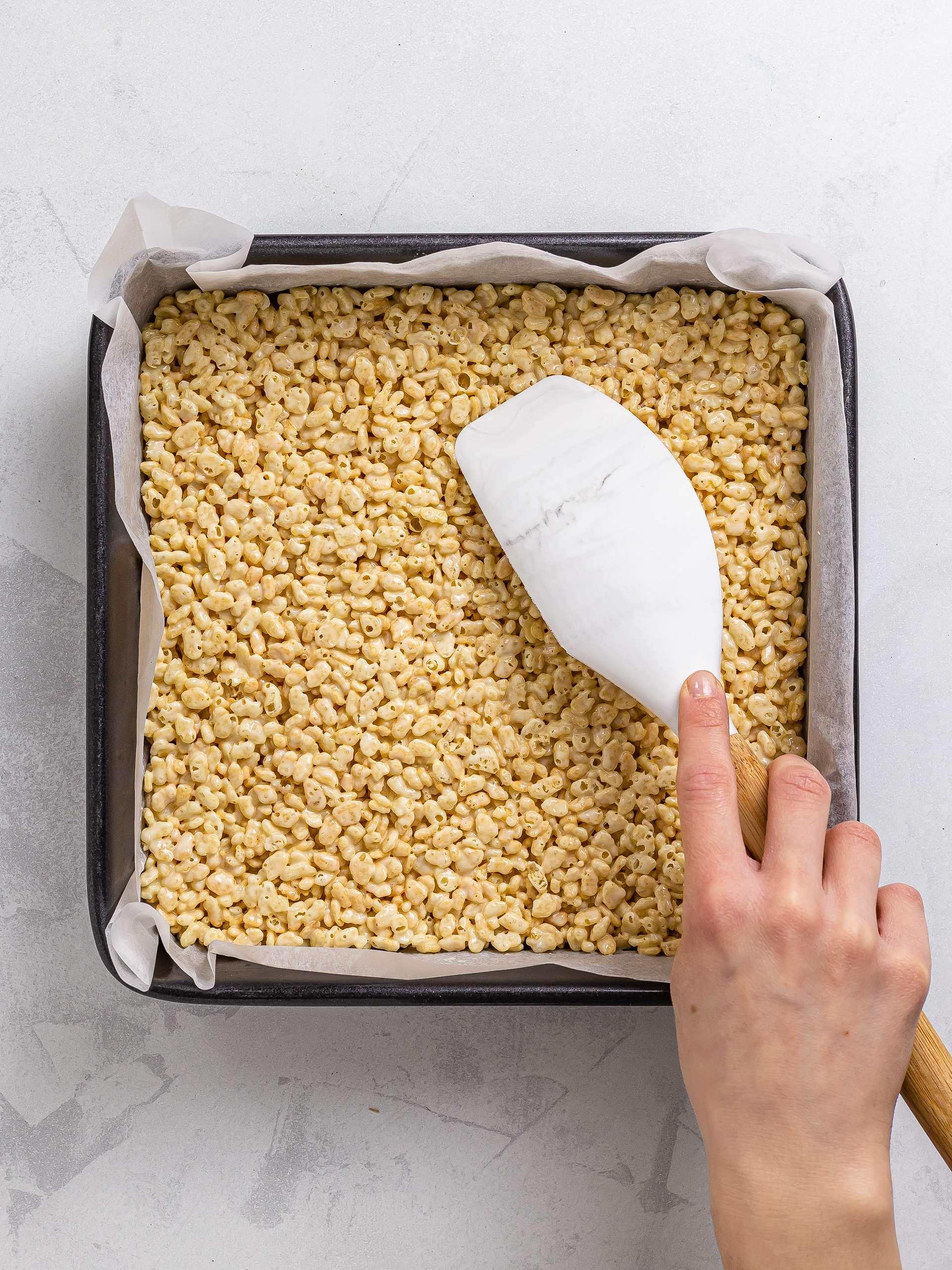 woman spreading rice crispies layer in a baking tin for ube bars