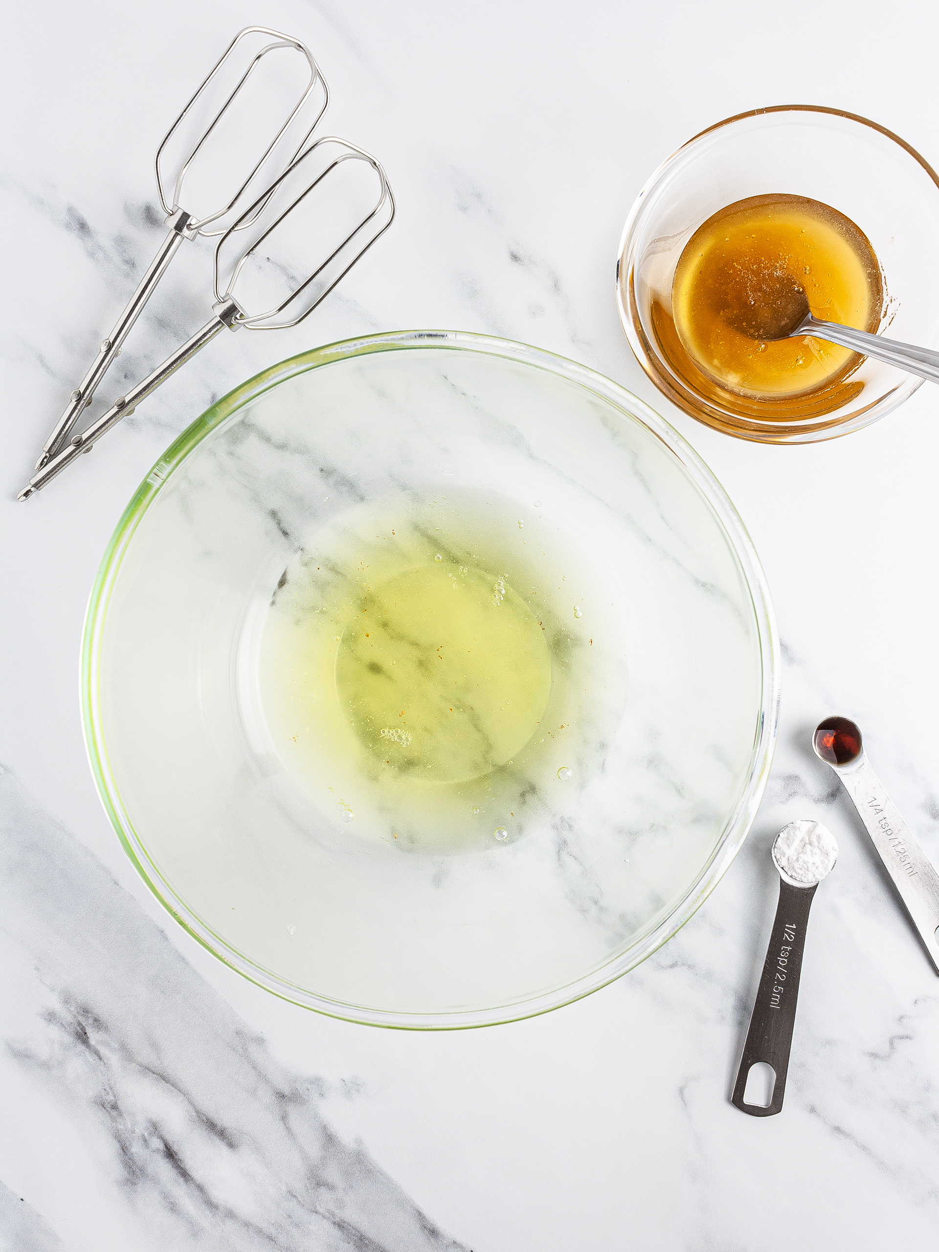 Egg whites in a bowl with vanilla, honey, and cream of tartar