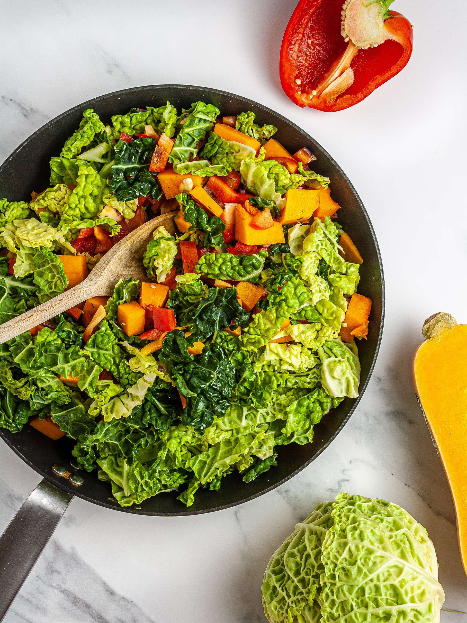 Cabbage, pumpkin, and red peppers cooking in a skillet.