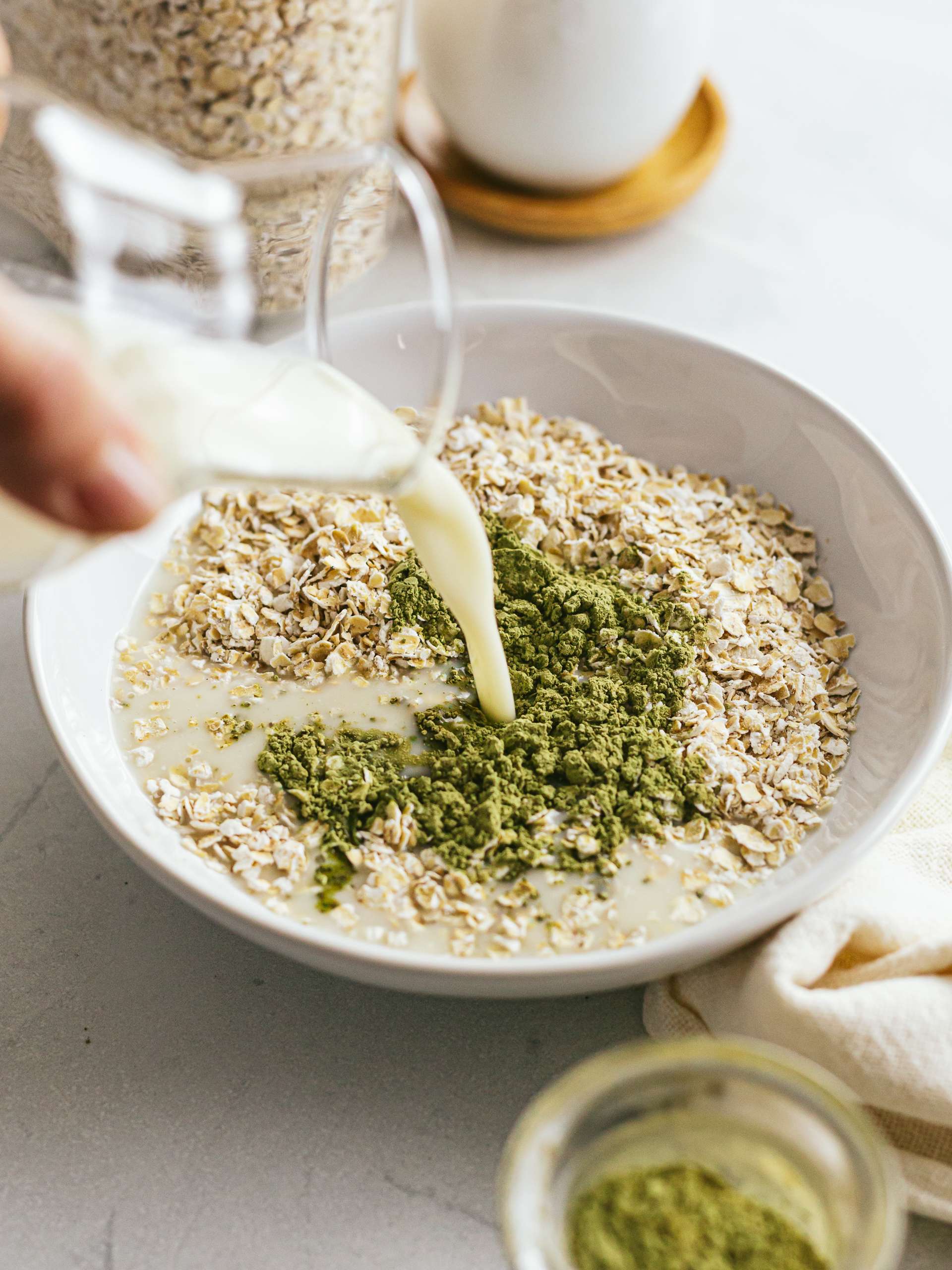 pouring milk into a bowl with oats and matcha powder