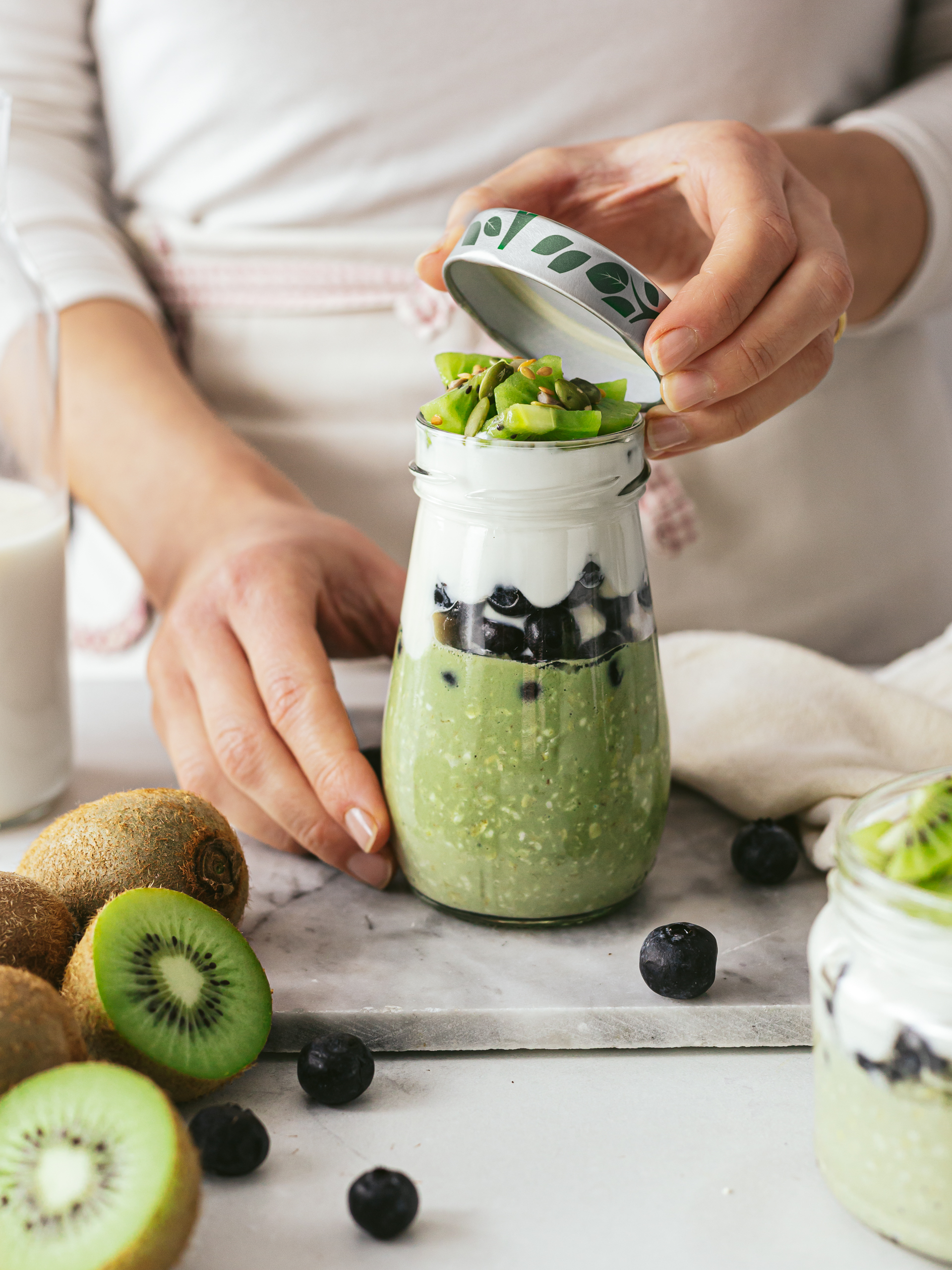 woman sealing a jar of matcha oats with yogurt, kiwi, berries, and seeds