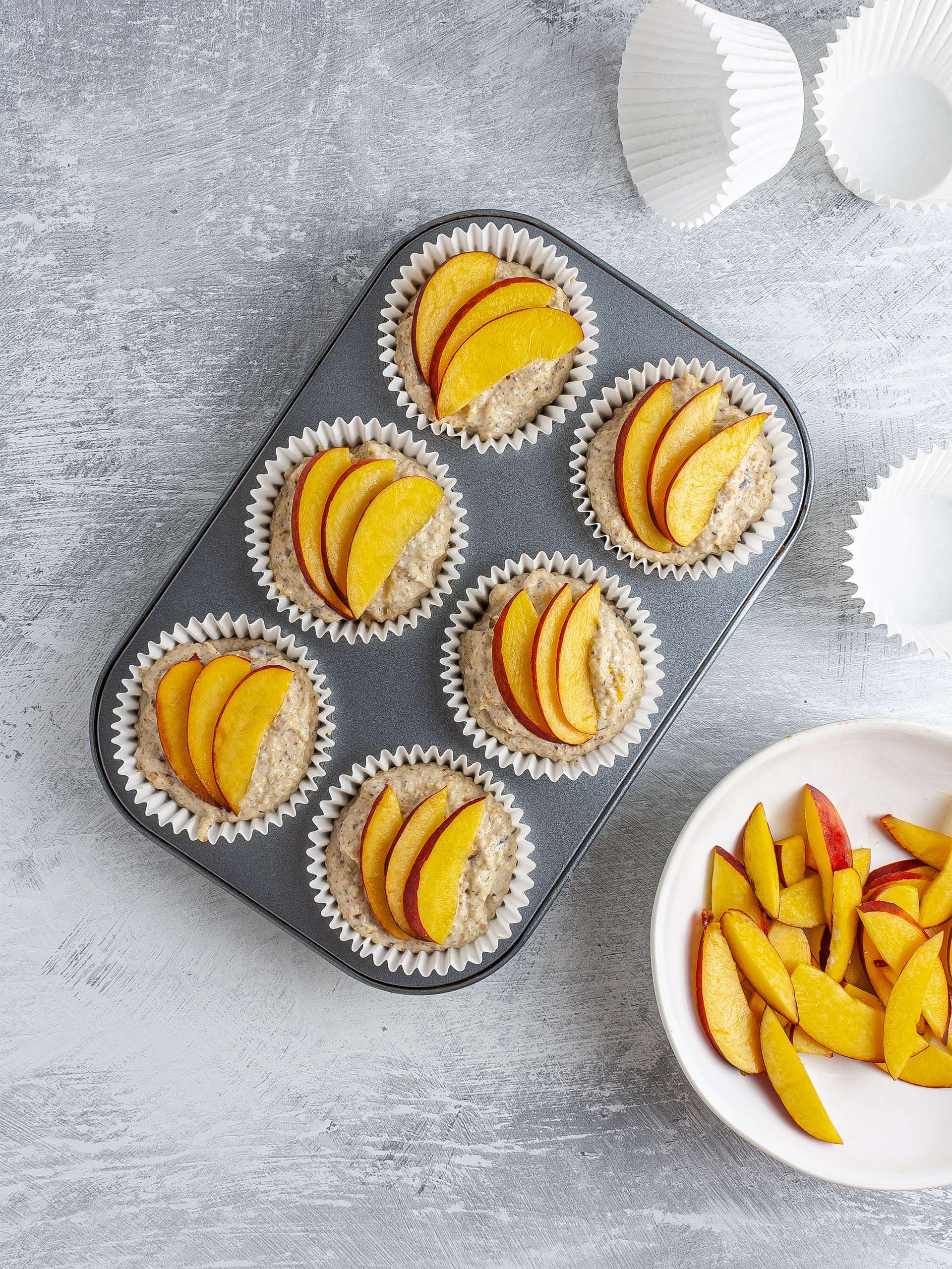 Muffin batter in cases topped with peach slices