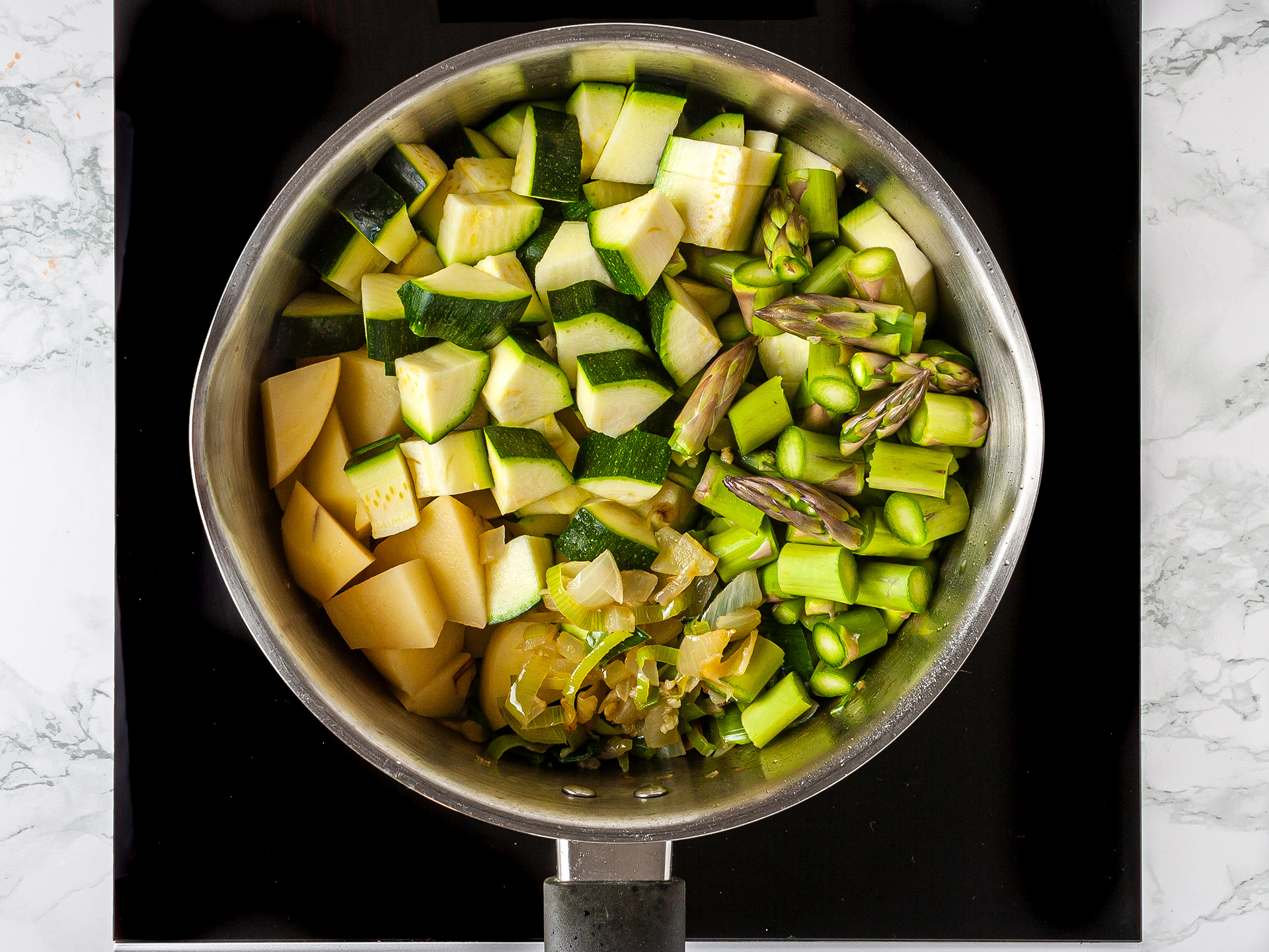 zucchini, potatoes, leeks, asparagus cooking in a pan
