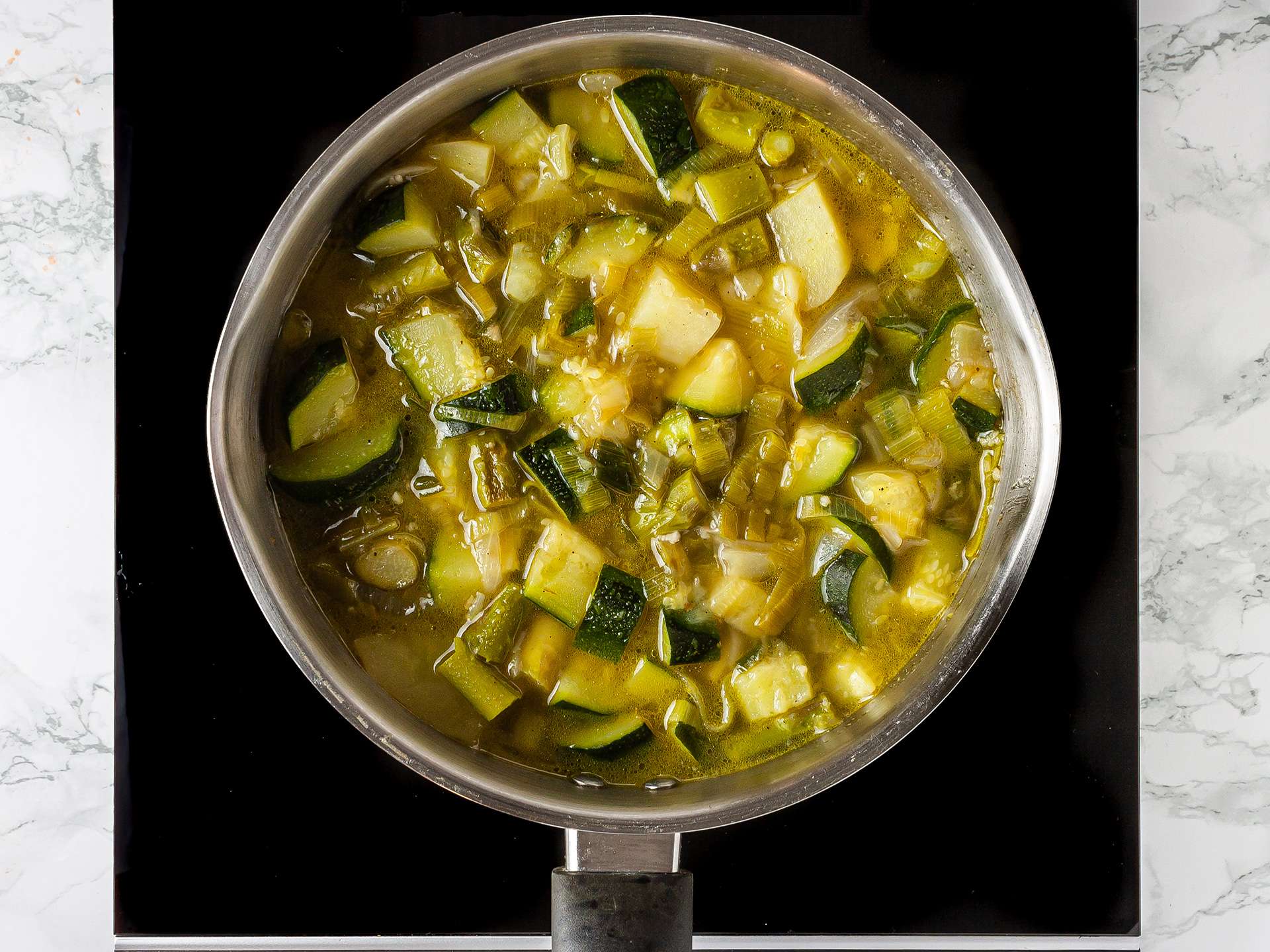 zucchini, asparagus, leek, and potato soup simmering in a pan