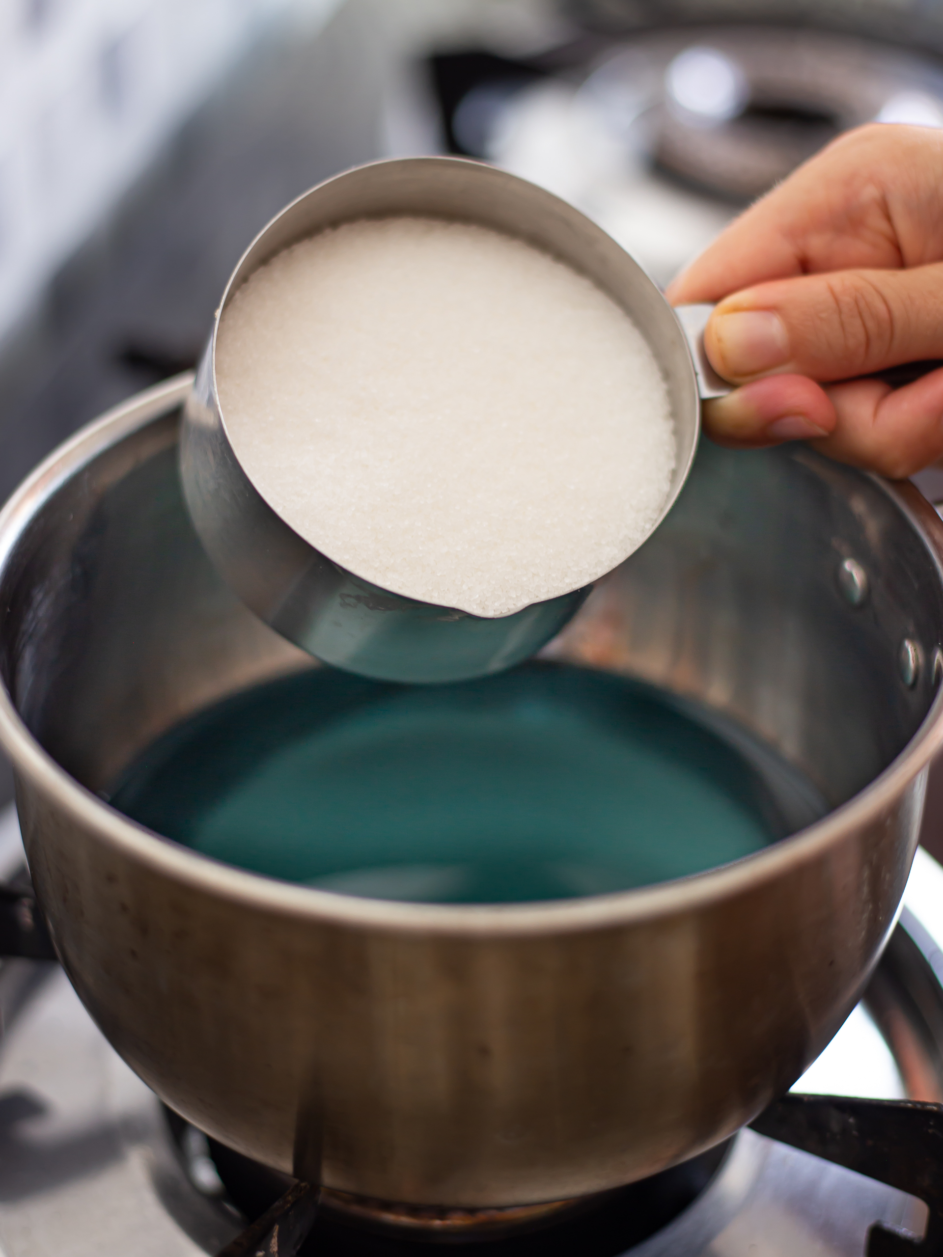 adding sugar to blue pea tea in a pot to make the syrup