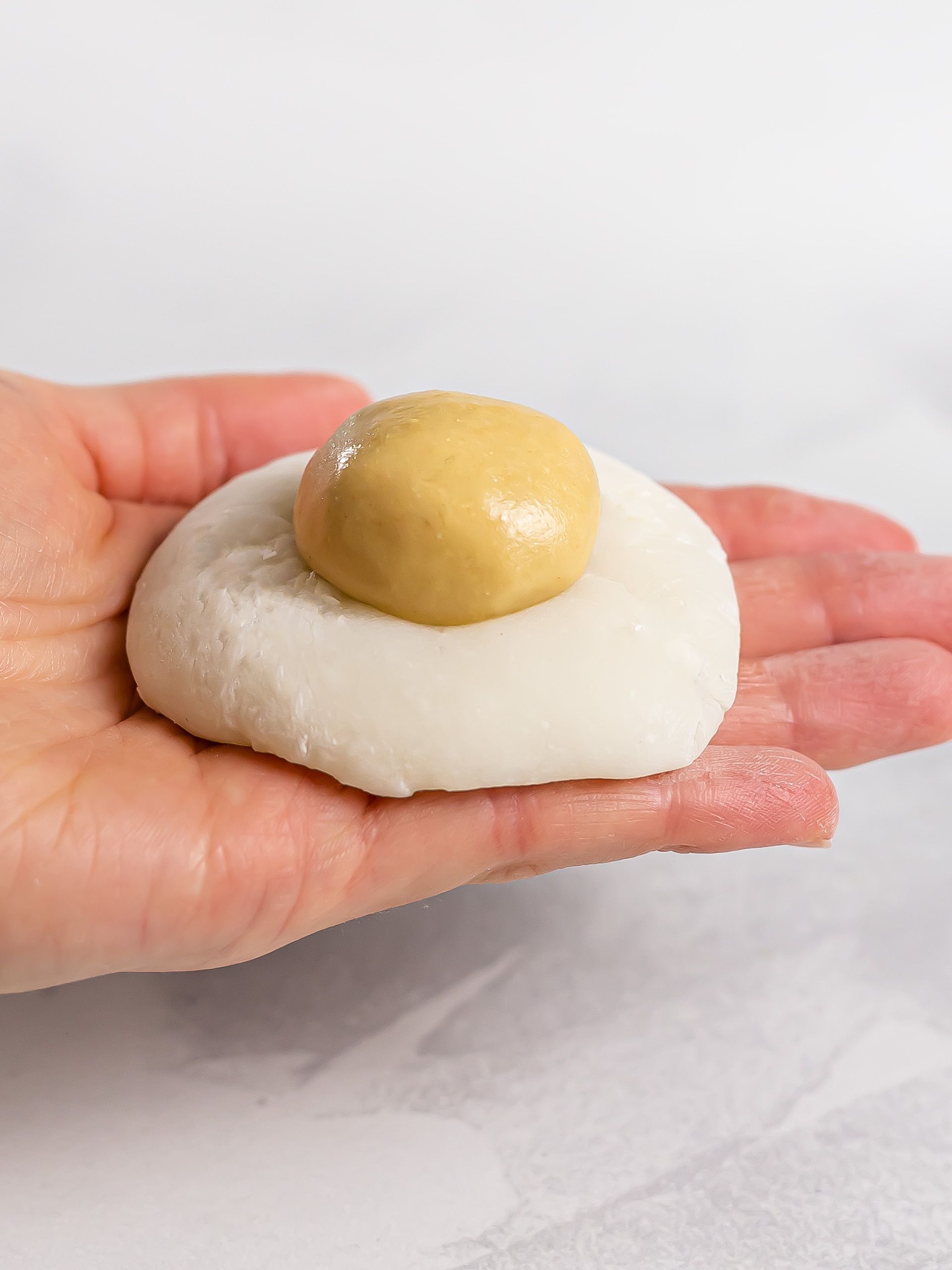 hand holding a mochi dough wrapper with peanut butter filling