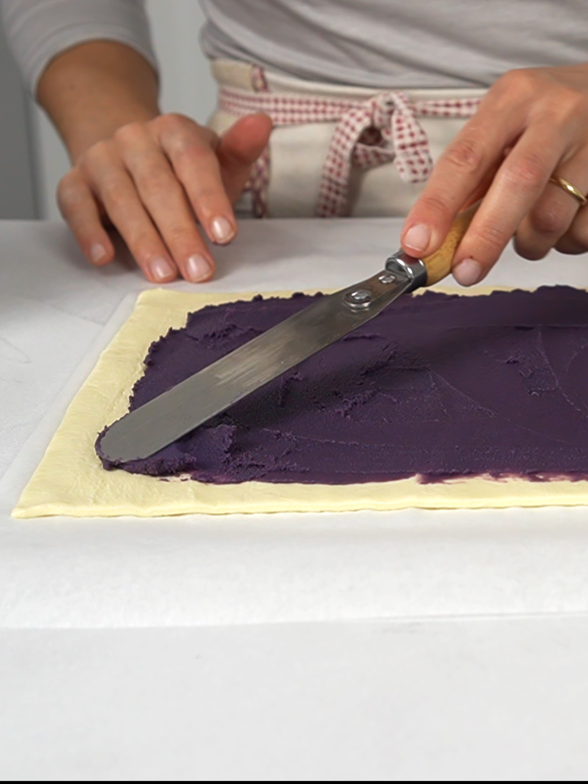woman spread ube butter on a sheet of puff pastry
