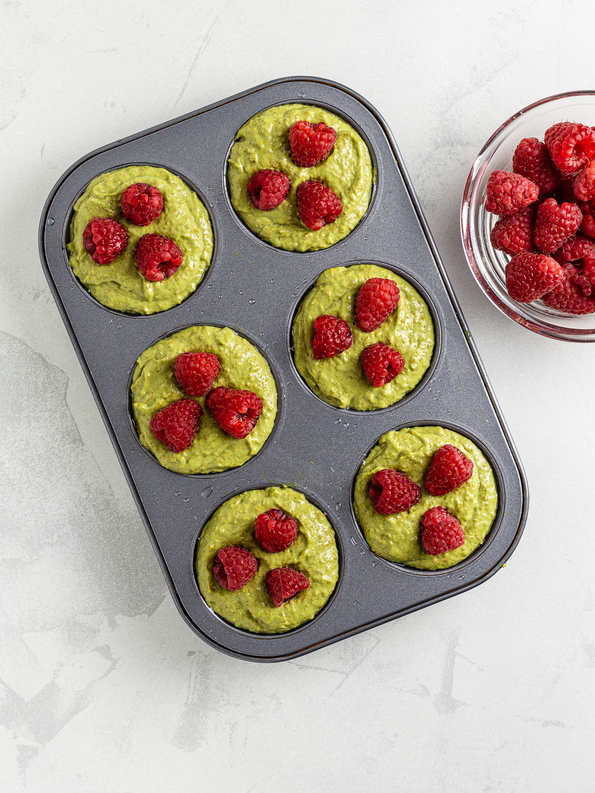 matcha muffins batter in a muffin tray with raspberries