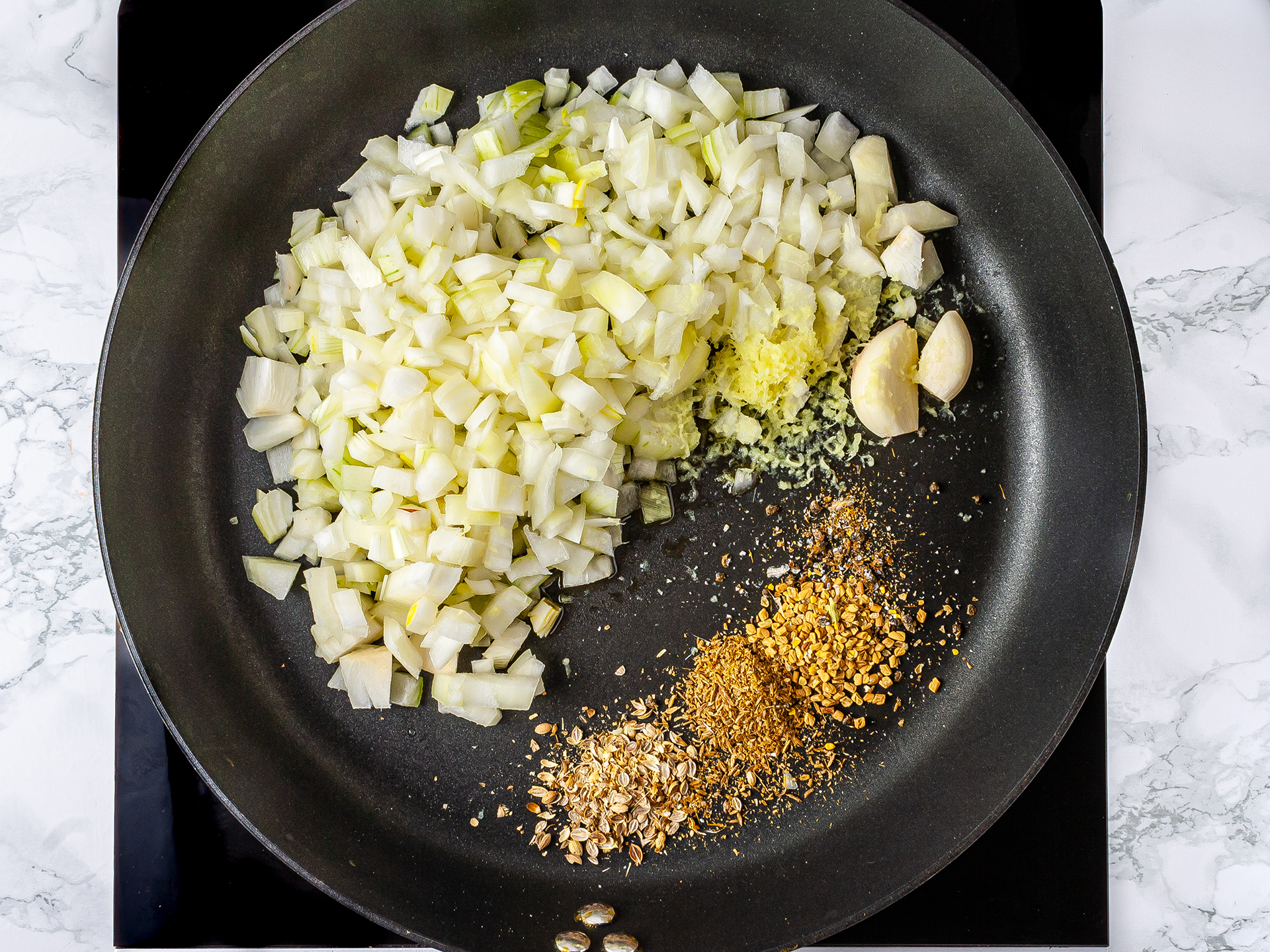 Onions, garlic, ginger root, cumin seeds, and coriander seeds sizzling in a pan.