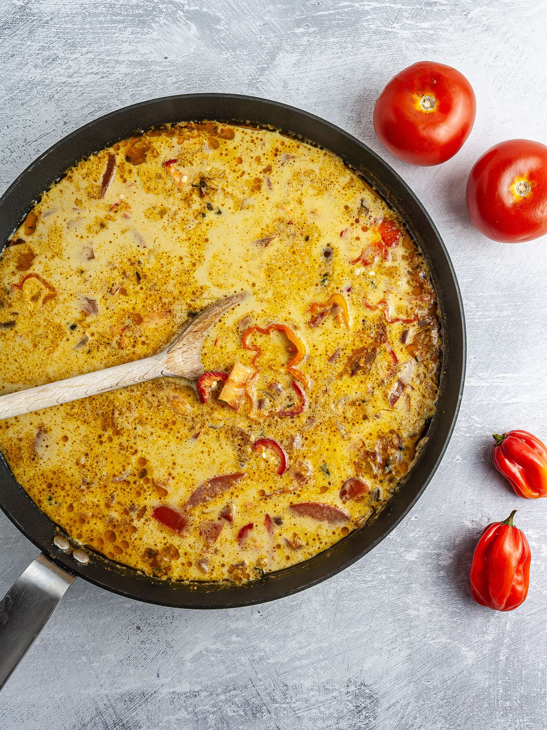 Coconut milk, tomatoes, and scotch bonnet chillies in a skillet