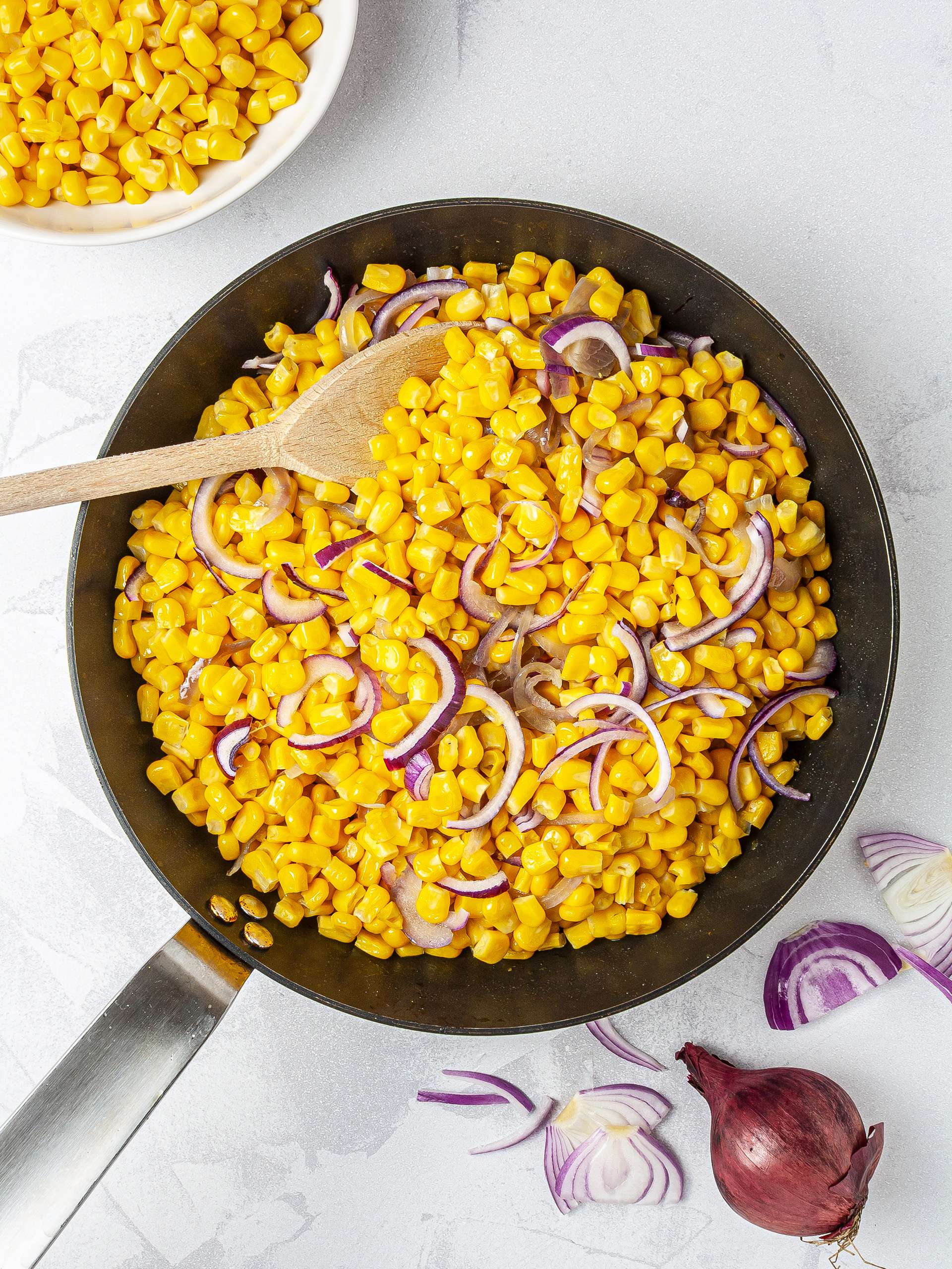 Sweet corn cooking in a pan with red onions.