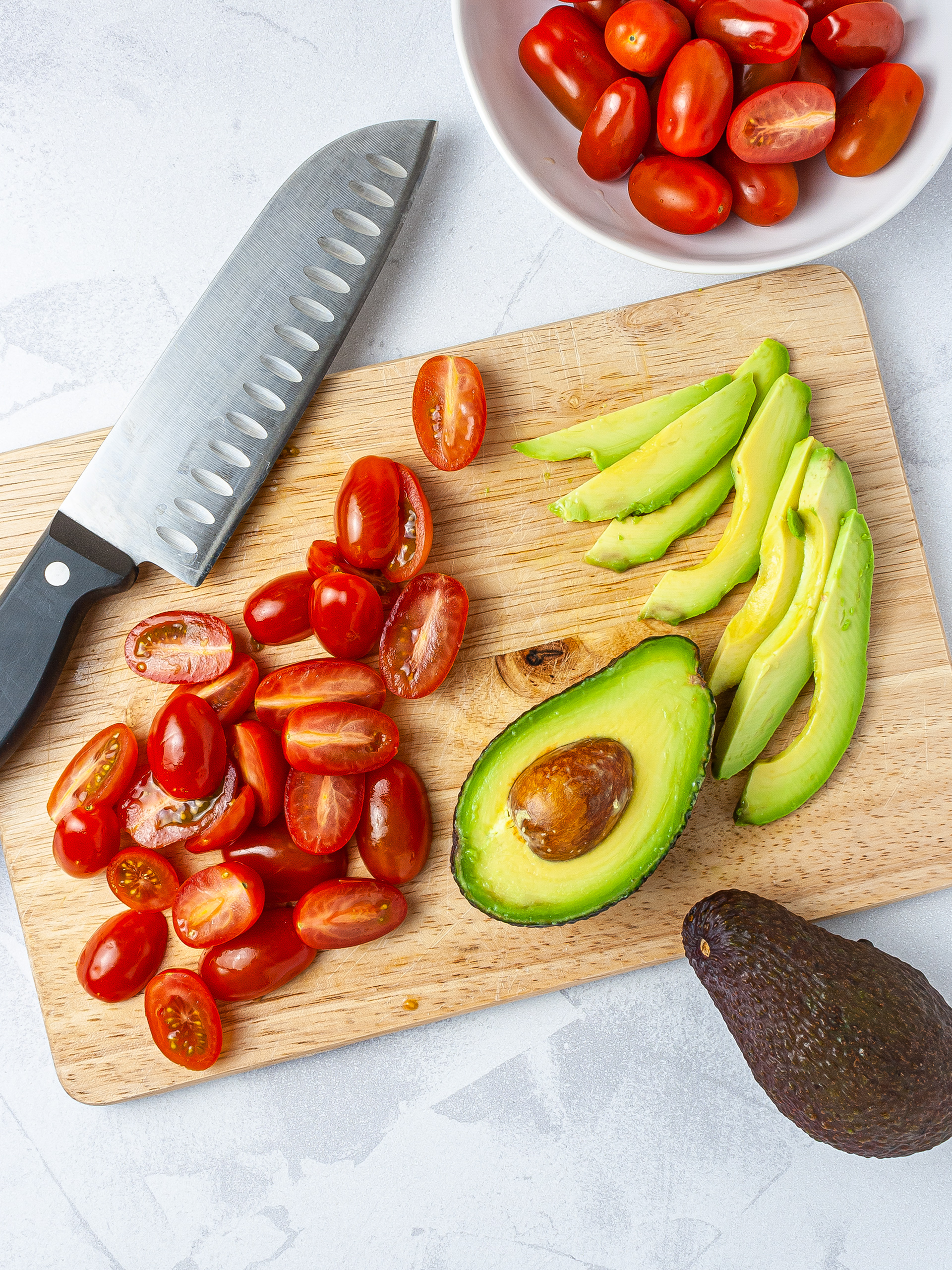 Halved tomatoes and sliced avocado on a chopping board.