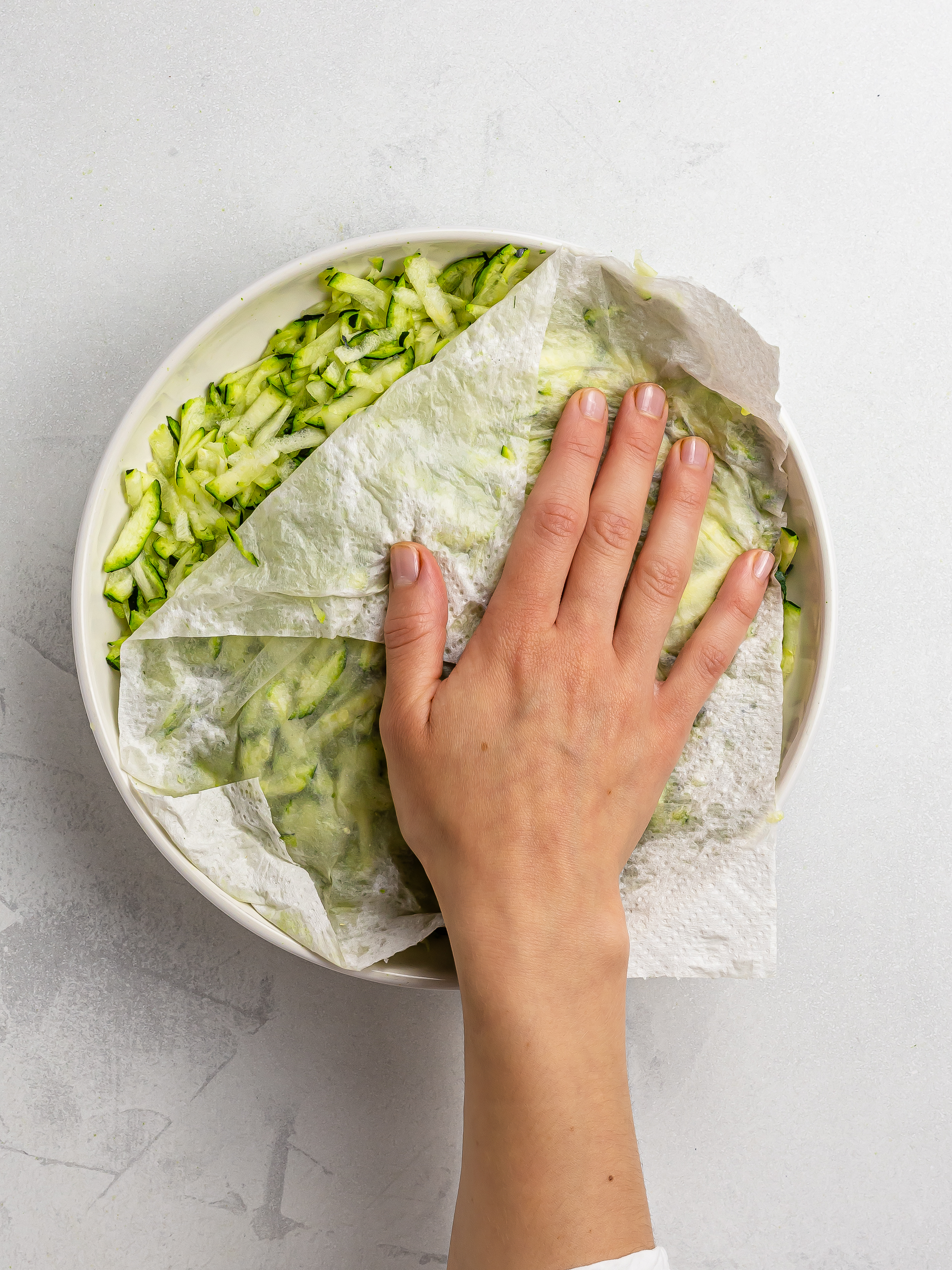 hand patting grated zucchini with kitchen paper