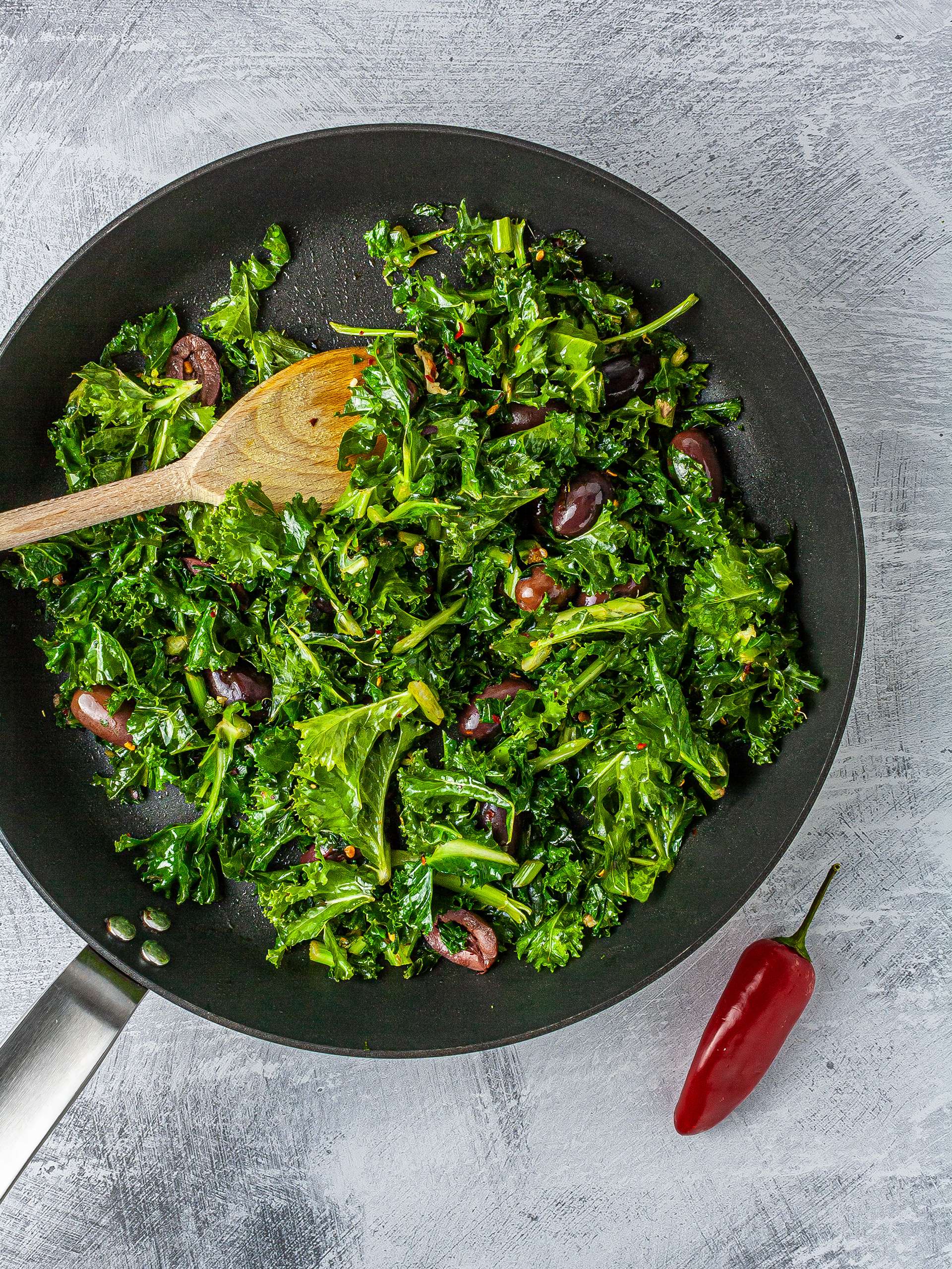 Kale cooked in a pan with chillies and olives.