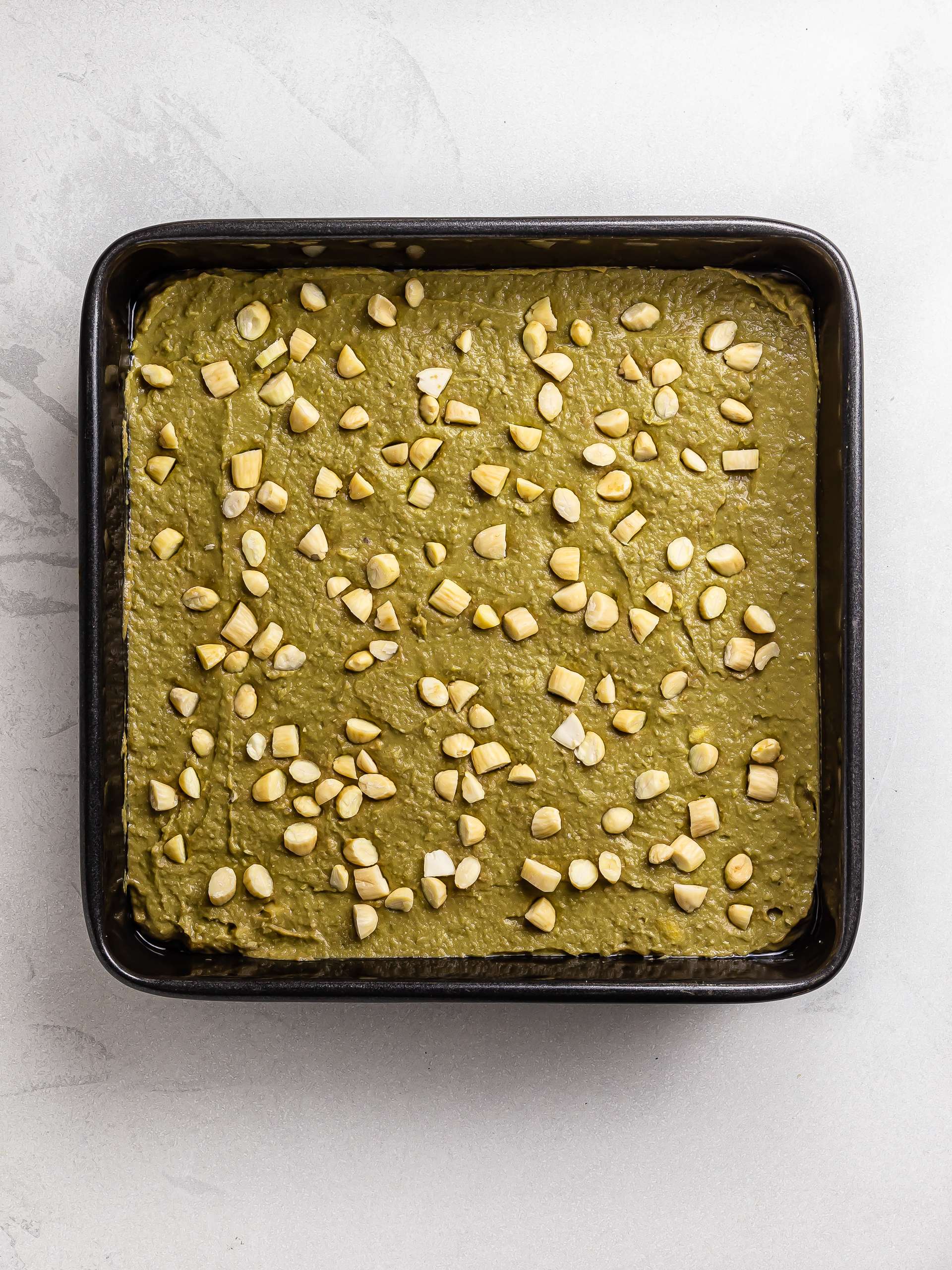 matcha brownies batter in a baking tin topped with almonds