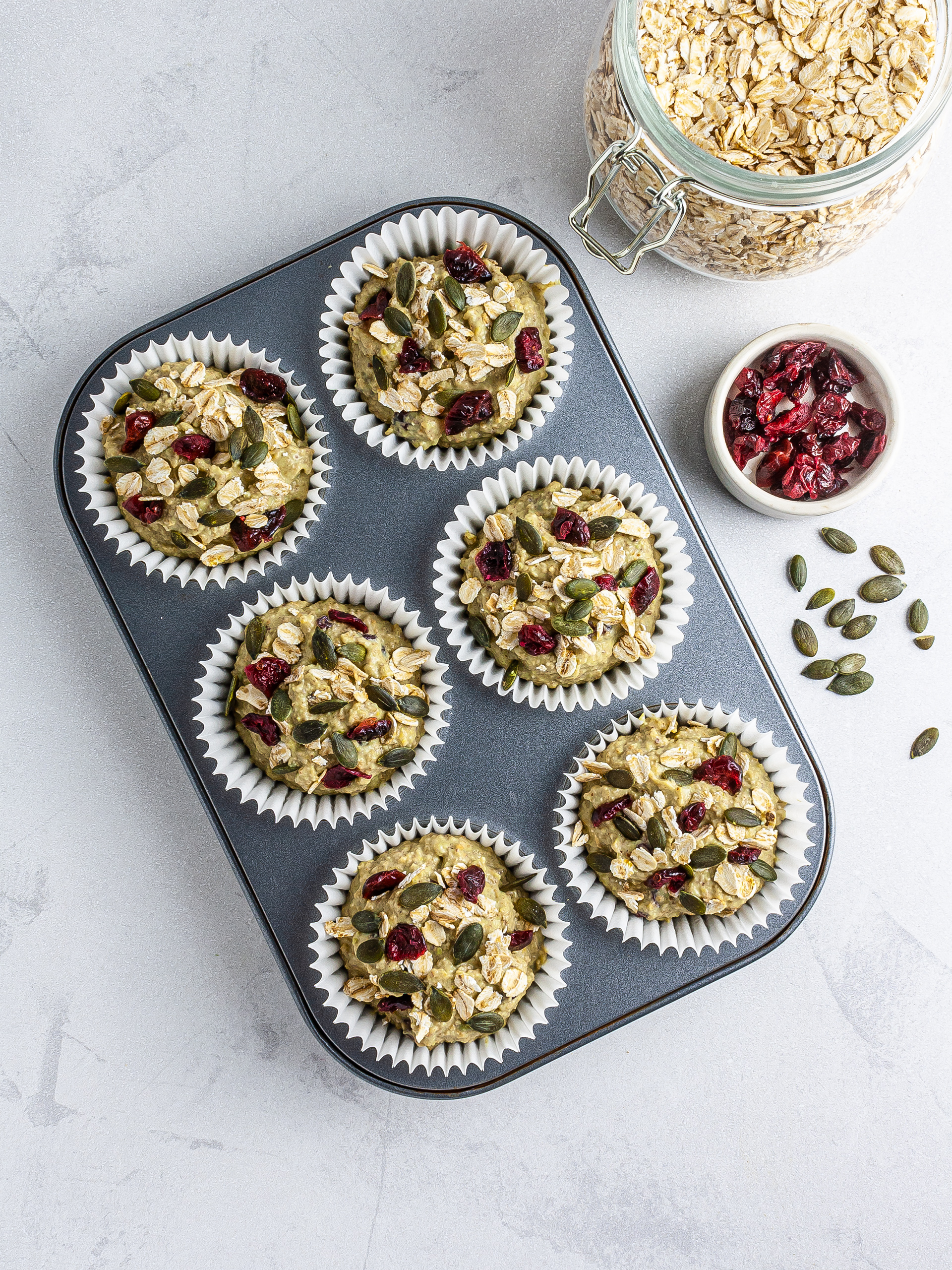 Muffin batter in muffin cases garnished with oats, pumpkin seeds and cranberries