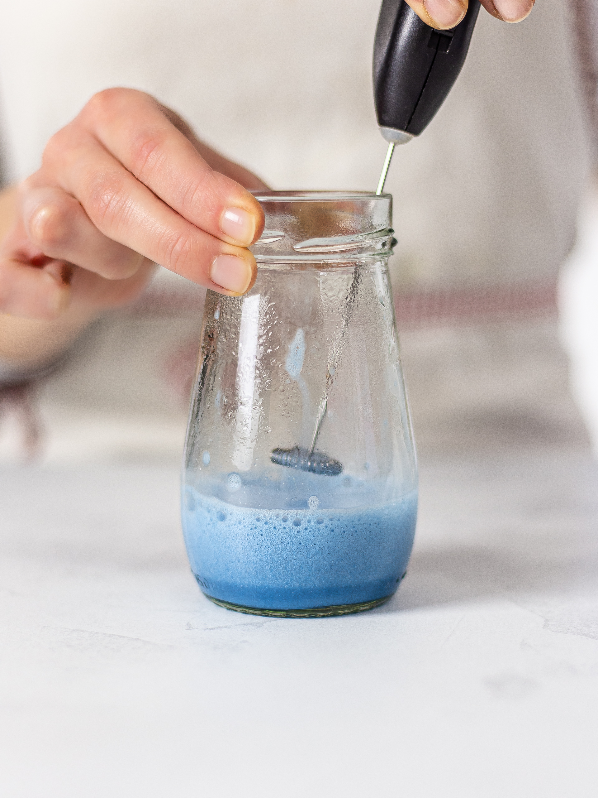 foaming butterfly pea latte with a hand frother