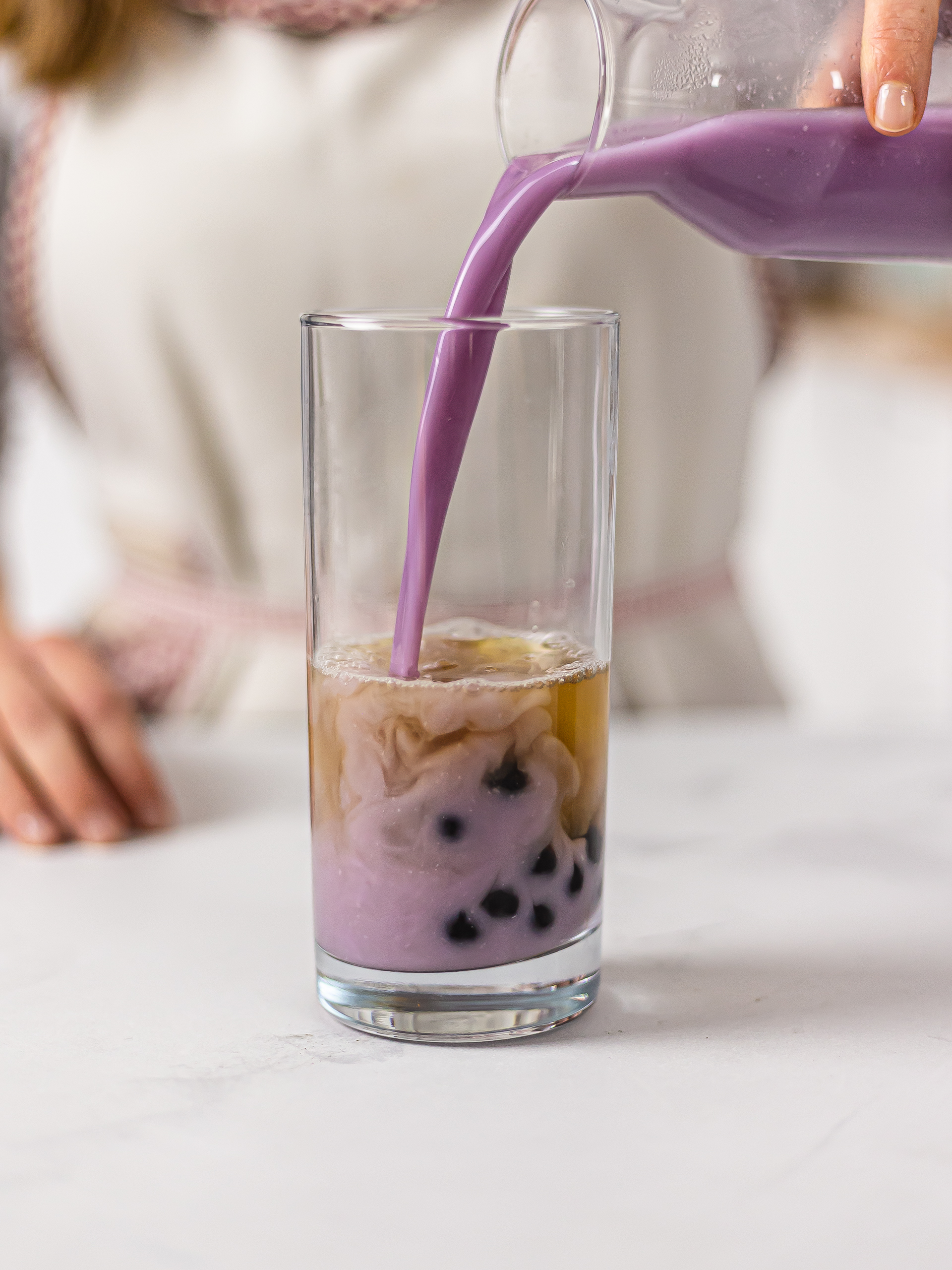 woman pouring ube milk into a glass with bubble tea