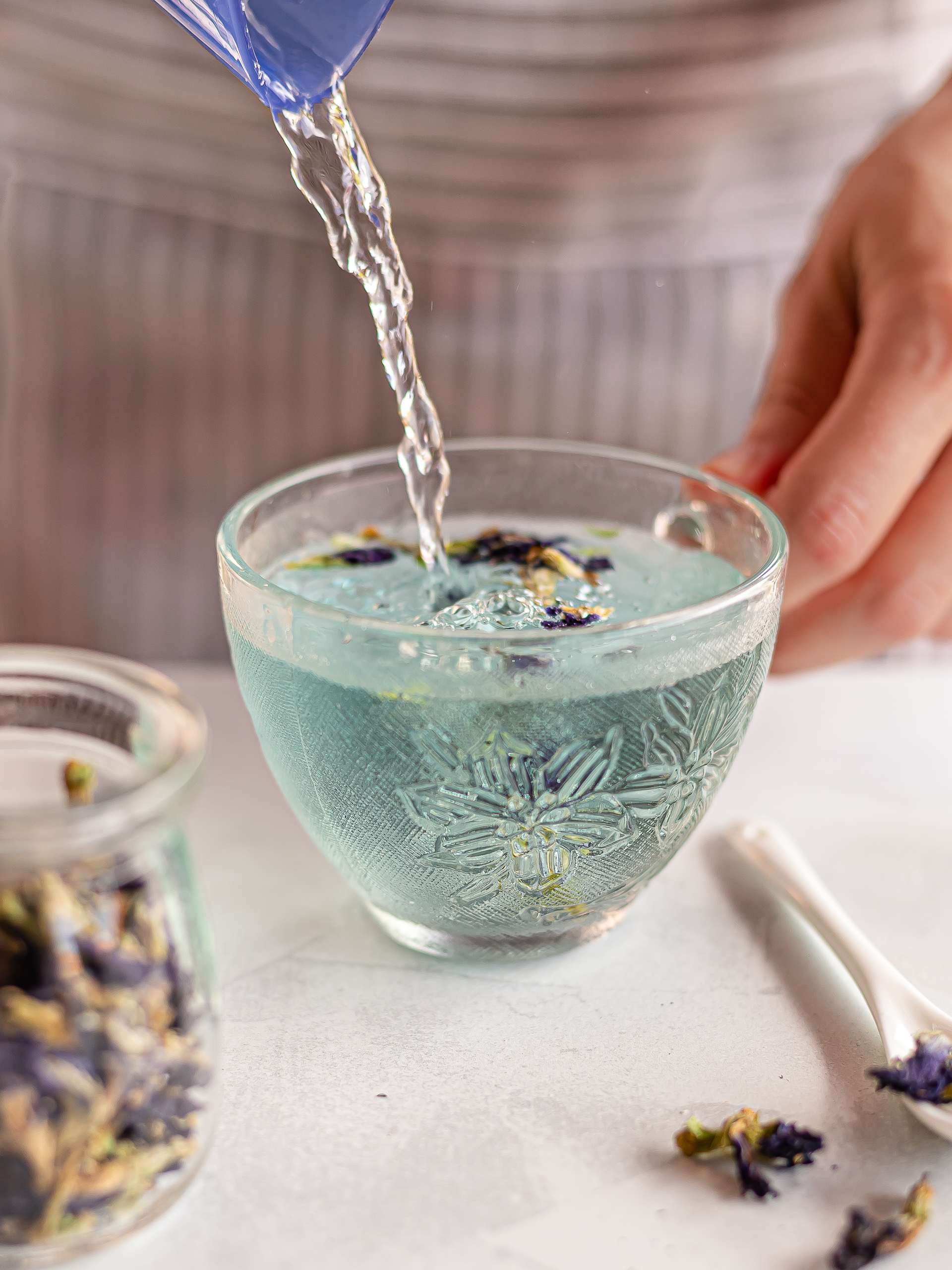 woman pouring hot water over butterfly pea flowers in a cup for tea